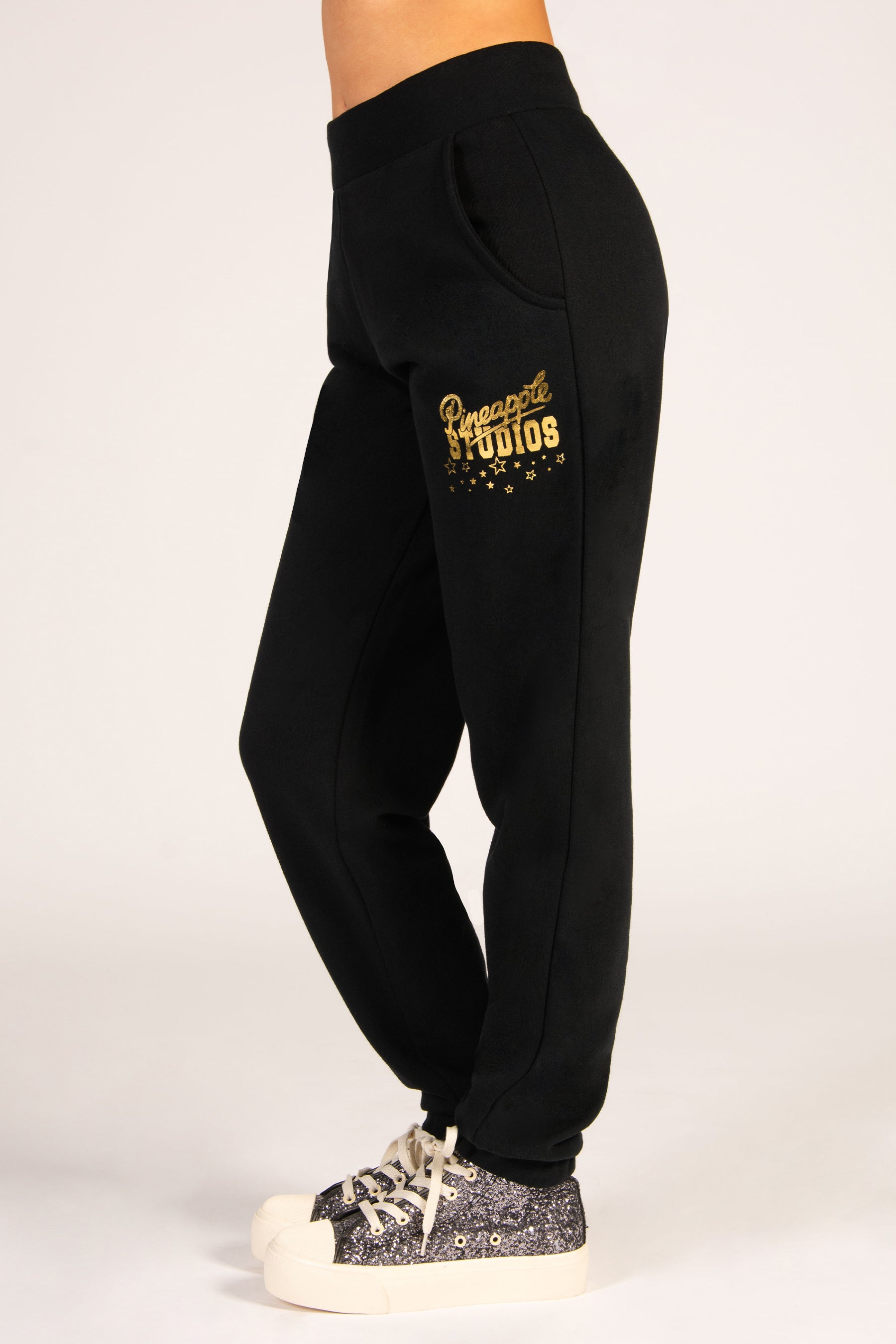 Girls' black joggers with side pockets, featuring a small Pineapple Studios gold foil print by the hip.