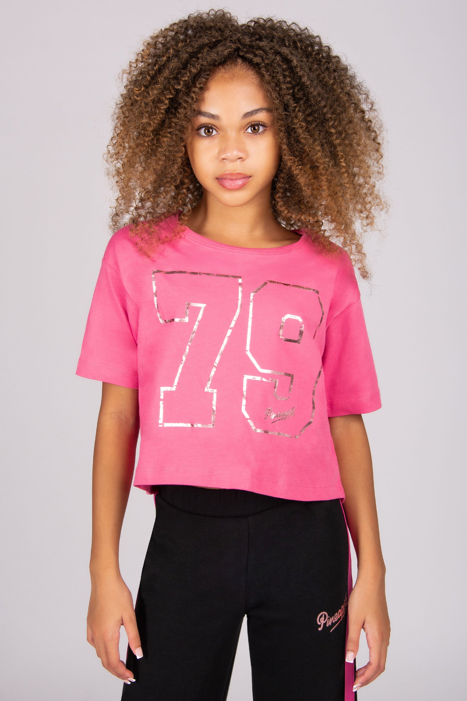Person wearing a pink t-shirt with the number 79 and black pants on a plain background