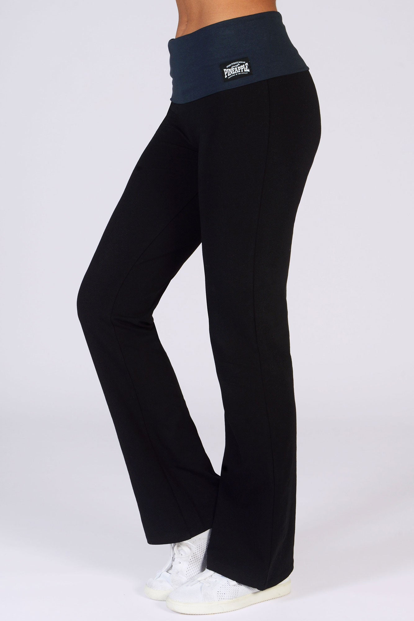 A pair of black jersey trousers with a fold waistband, displayed on a model facing to the side, wearing white sneakers.