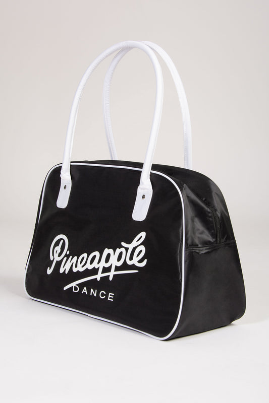 Black bag with white handle and 'Pineapple Dance' text on a light grey background