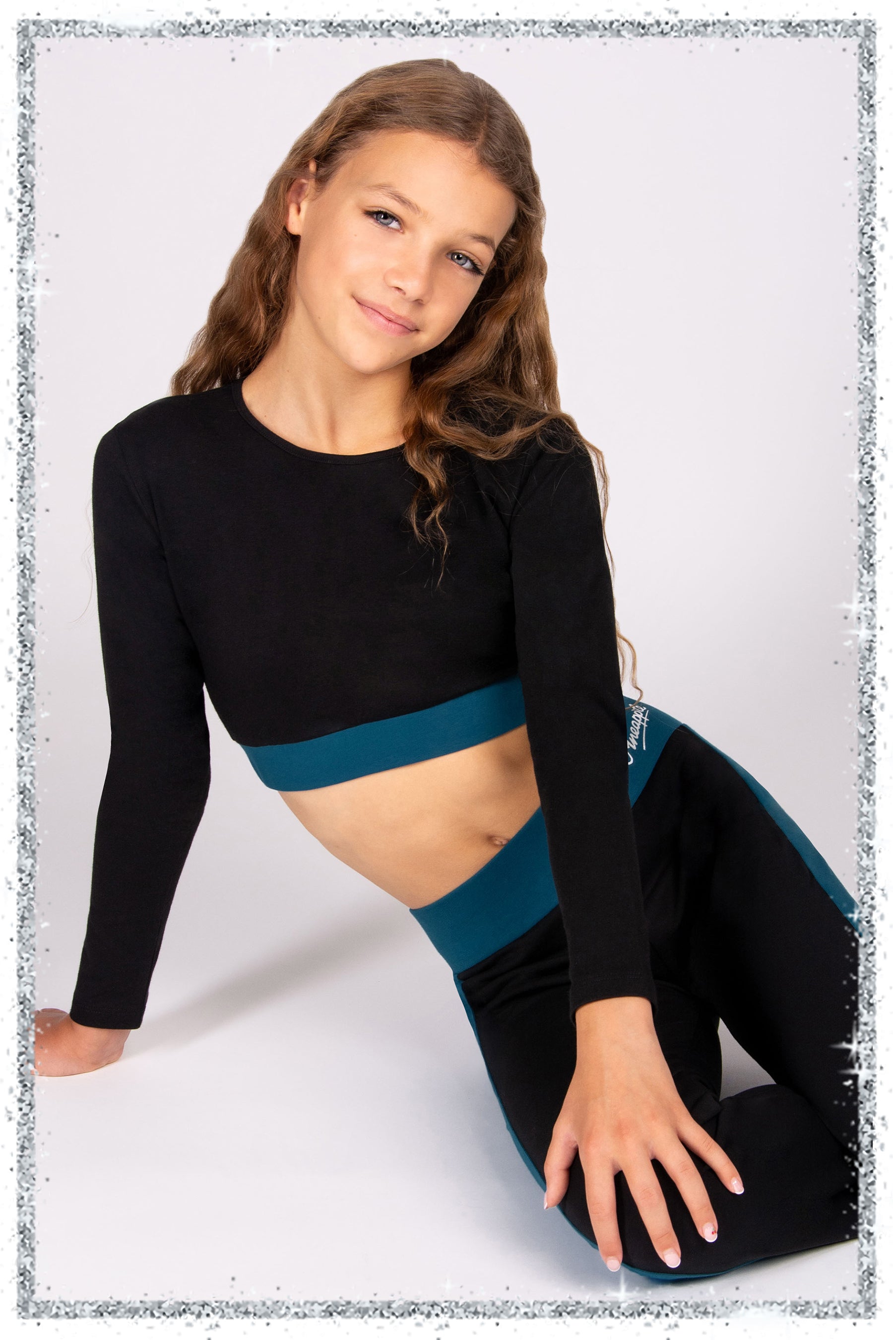 girls wearing a black long sleeve fitted crop top with matching trousers on a grey background.