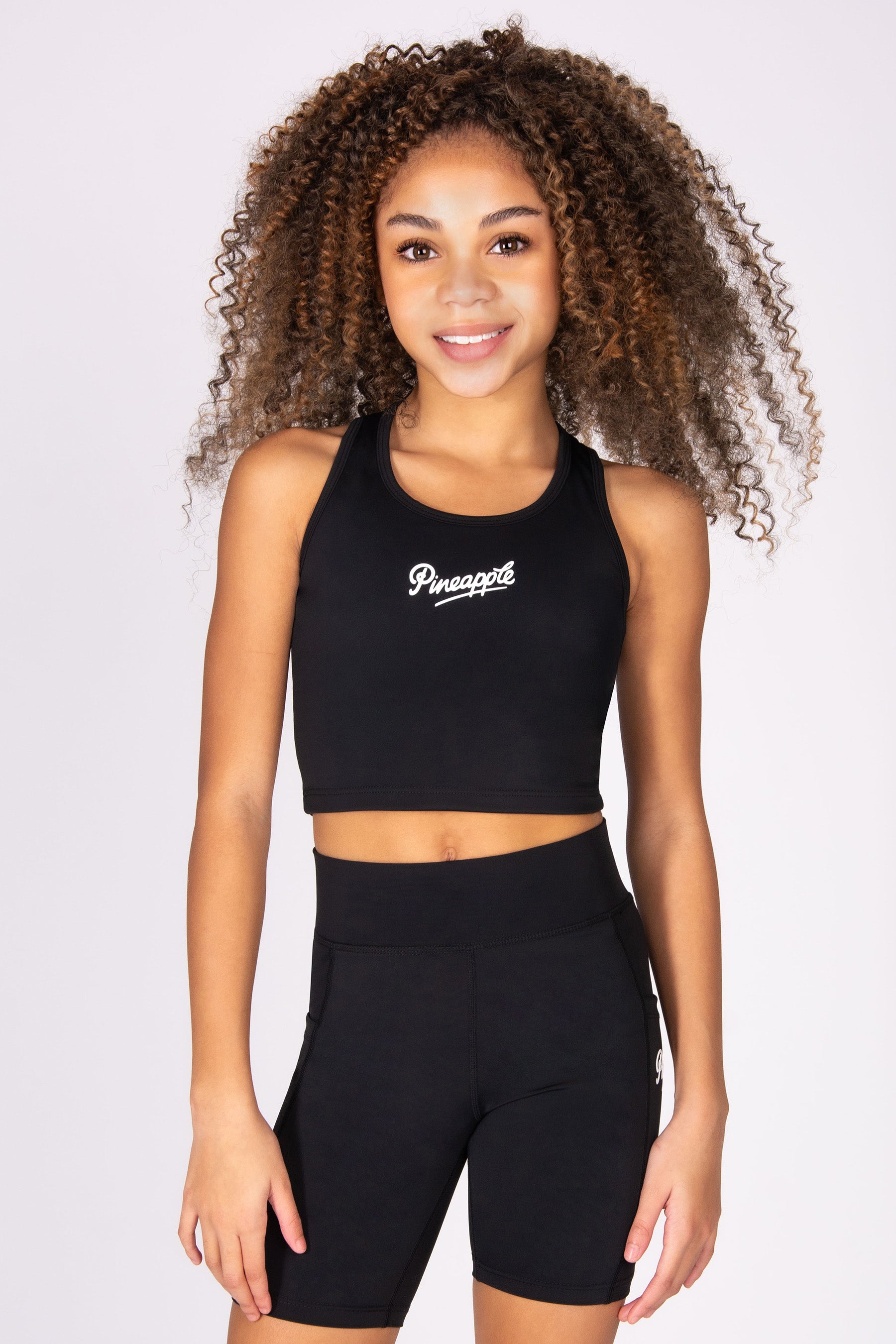 Girl wearing a black active vest top with cycling shorts on a light grey background