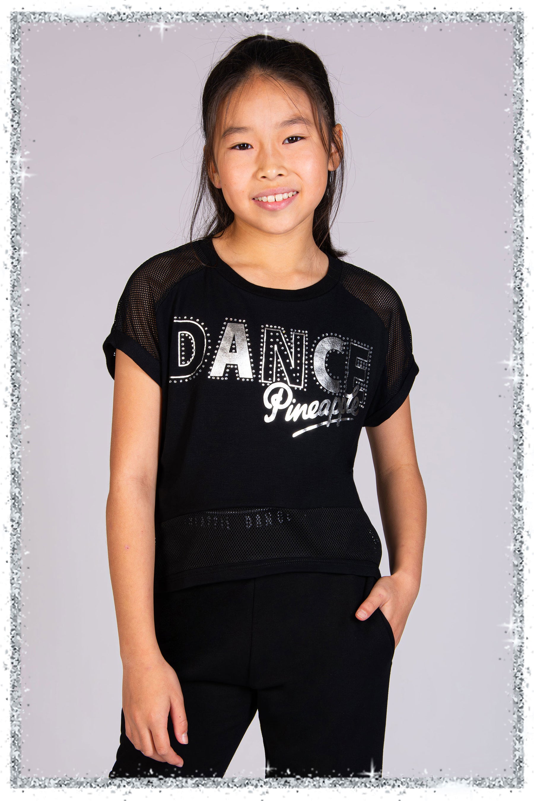 Young girl wearing a black 'DANCE Pineapple' t-shirt on a gray background