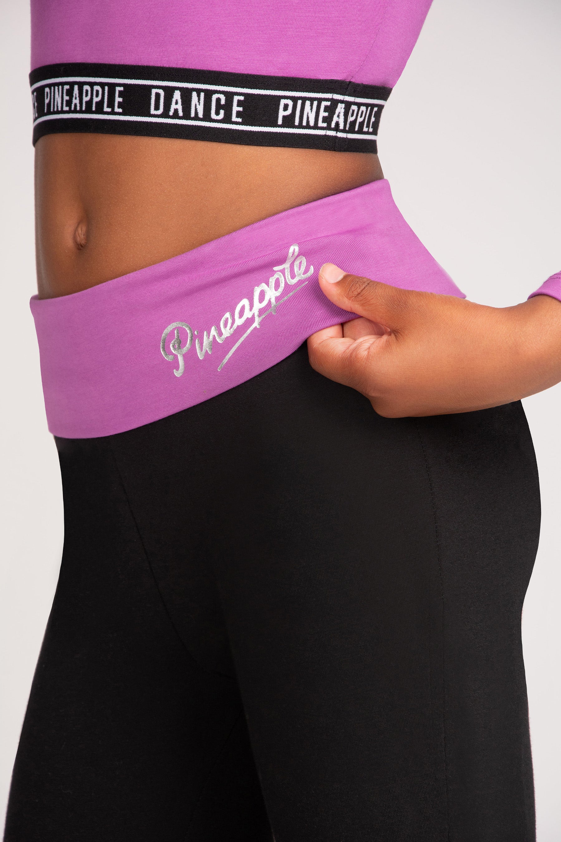 A close-up of a person wearing a light purple athletic waistband with the brand name 'Pineapple' in silver foil, paired with black leggings. 