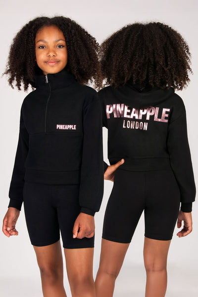 Black hoodie and shorts set with 'Pineapple London' branding worn by a model on a white background