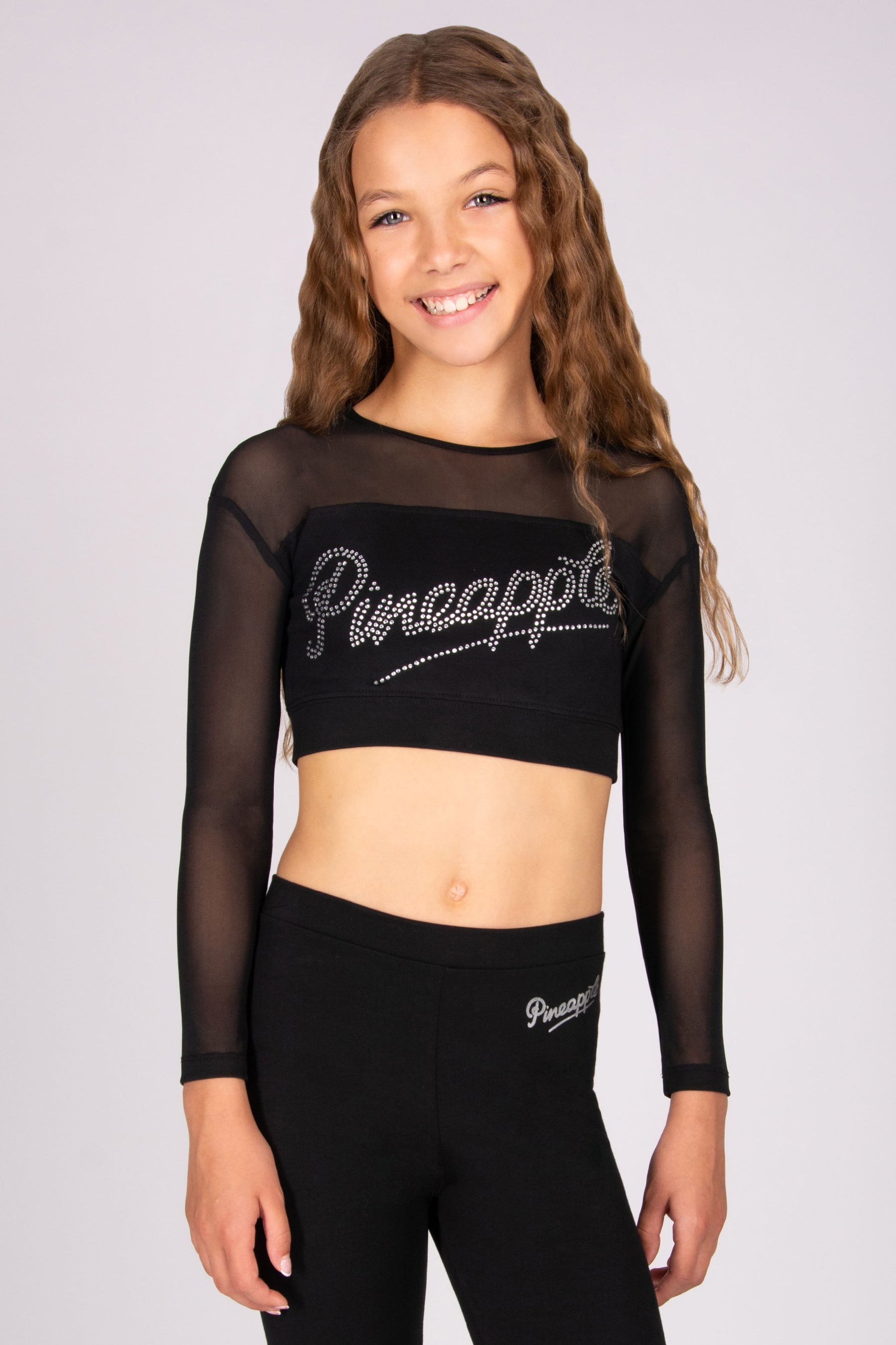 Girl wearing a black 'Pineapple' crop top with mesh sleeves and leggings on a light grey background