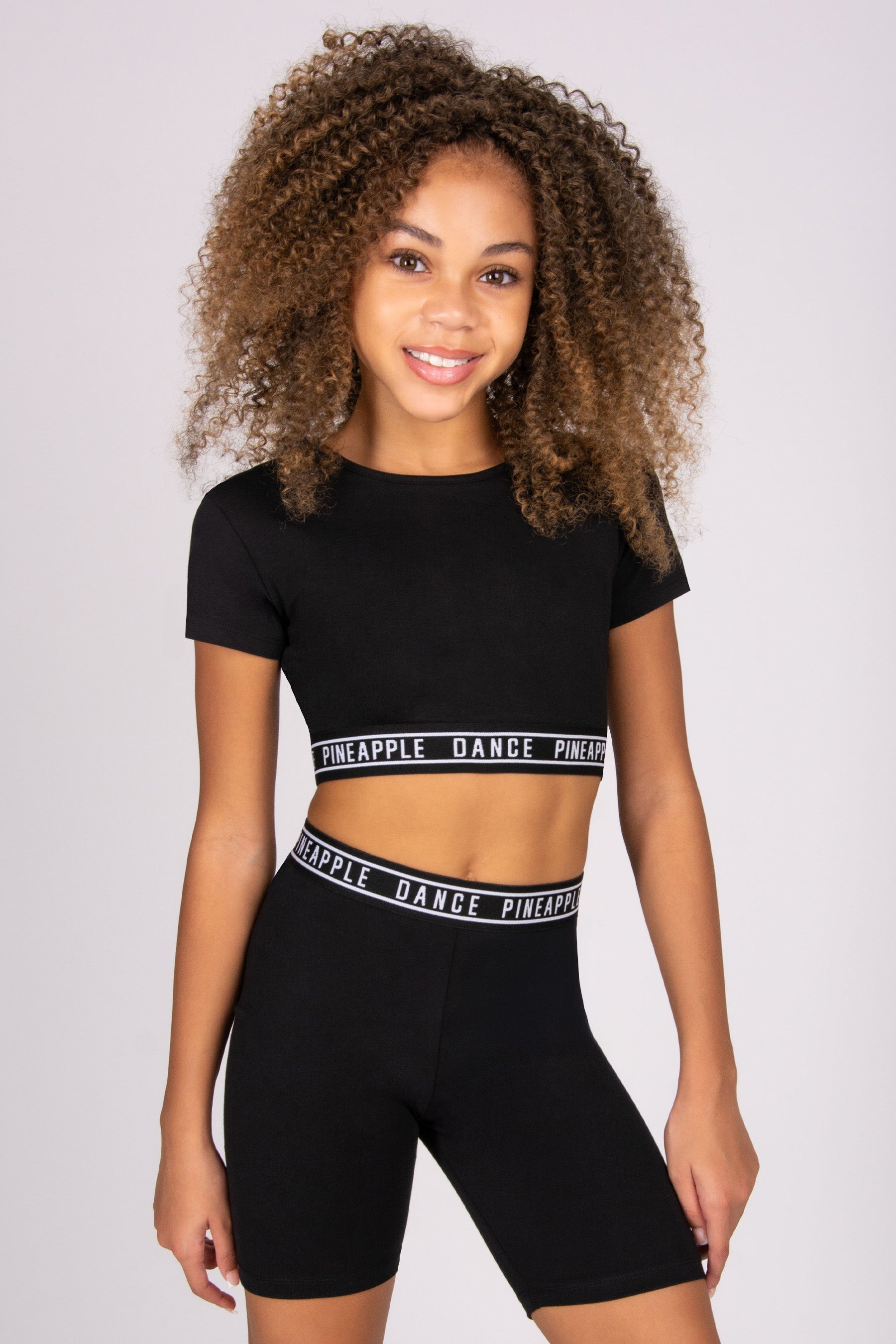 Person wearing a black crop top and black shorts with Pineapple Dance branding on a plain background