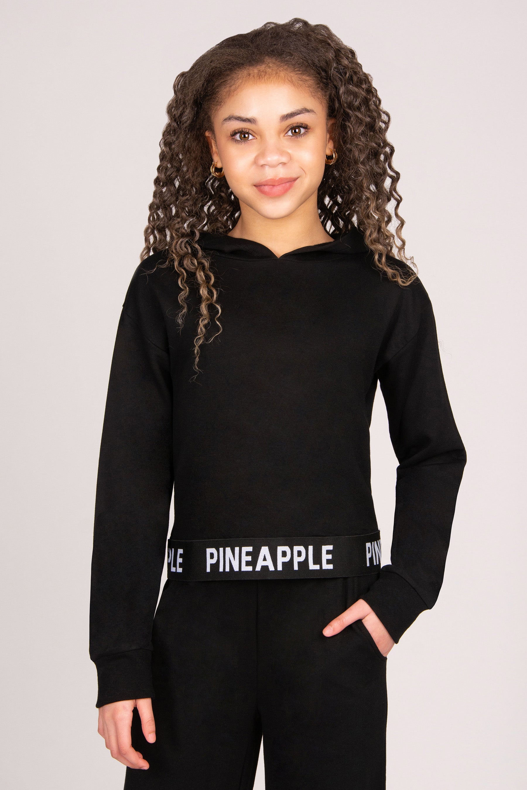 Girl wearing a black lightweight hoodie with 'Pineapple Dance' tape hem.