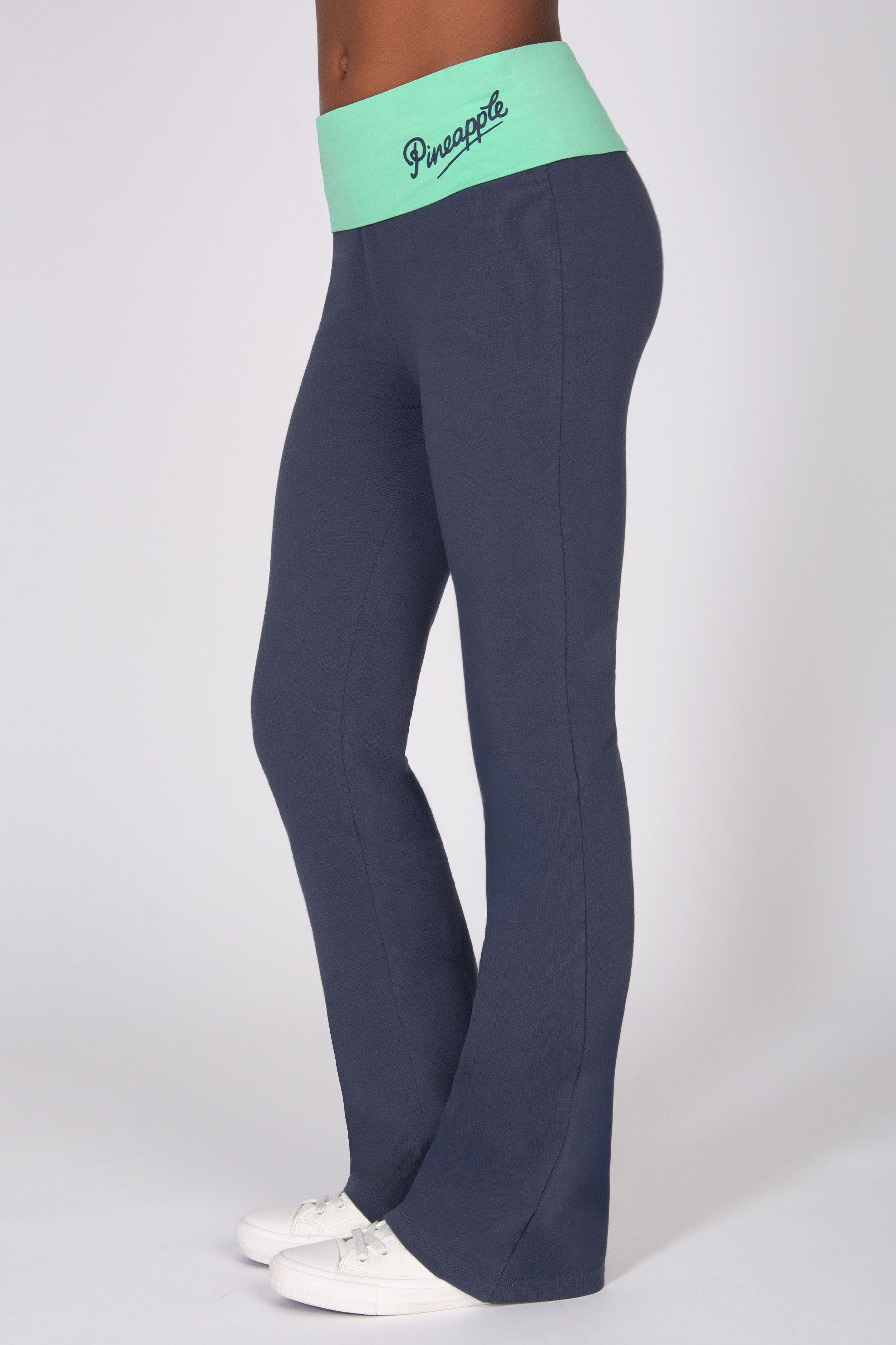 Girl wearing a dark grey flared jersey trousers with mint green fold-over waistband on a white background