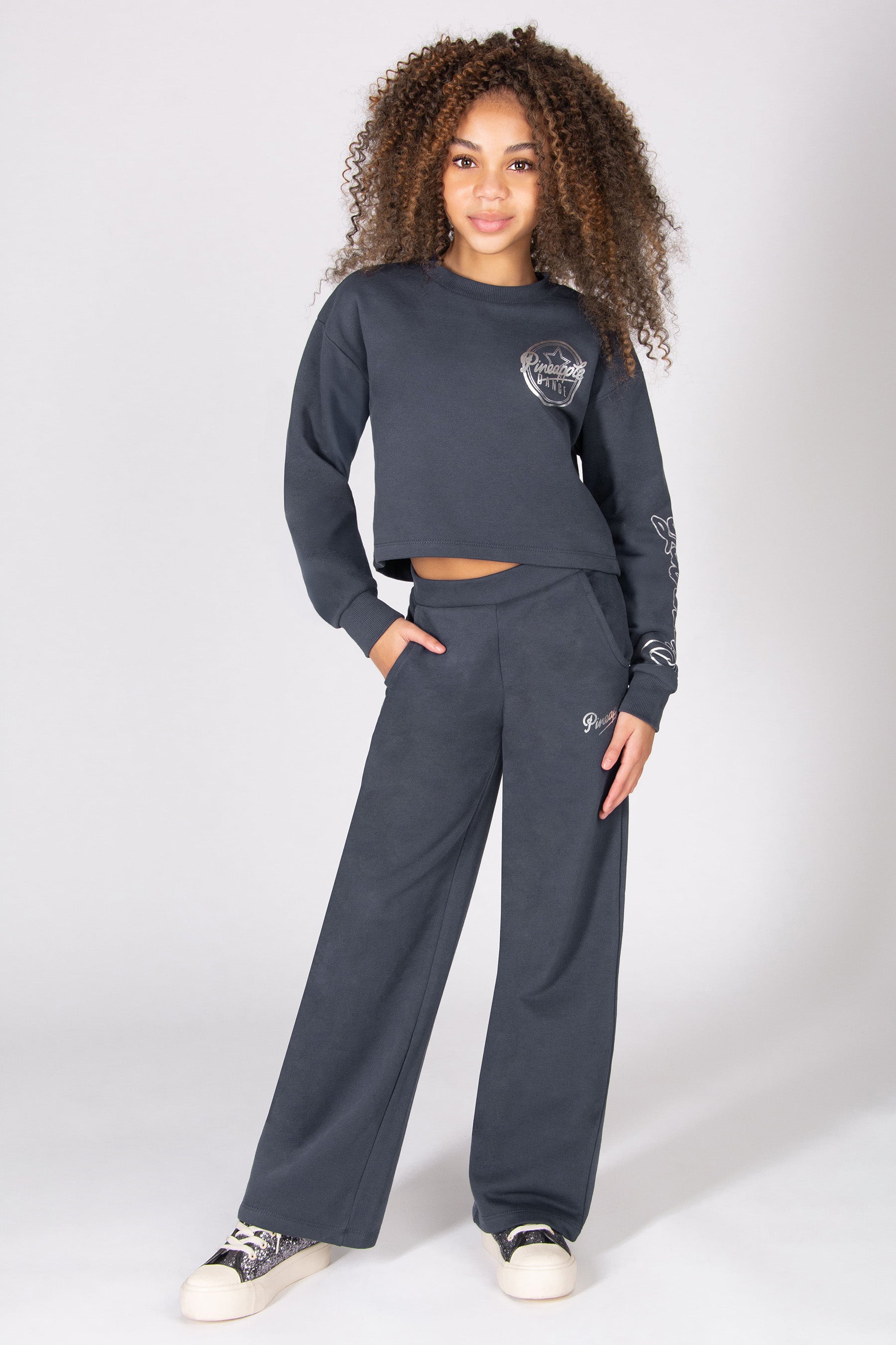 Girl wearing a dark grey sweatshirt and wide leg trousers set on a white background