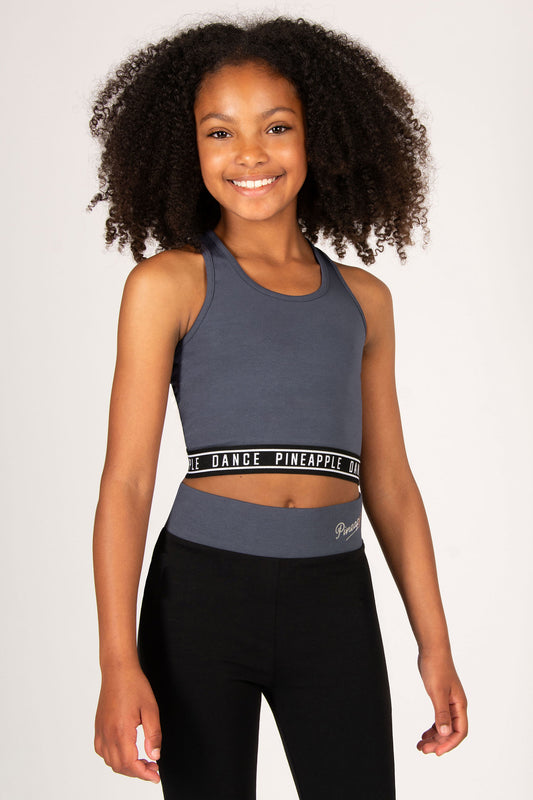 Young girl wearing a dark grey tank top and black flares on a plain background