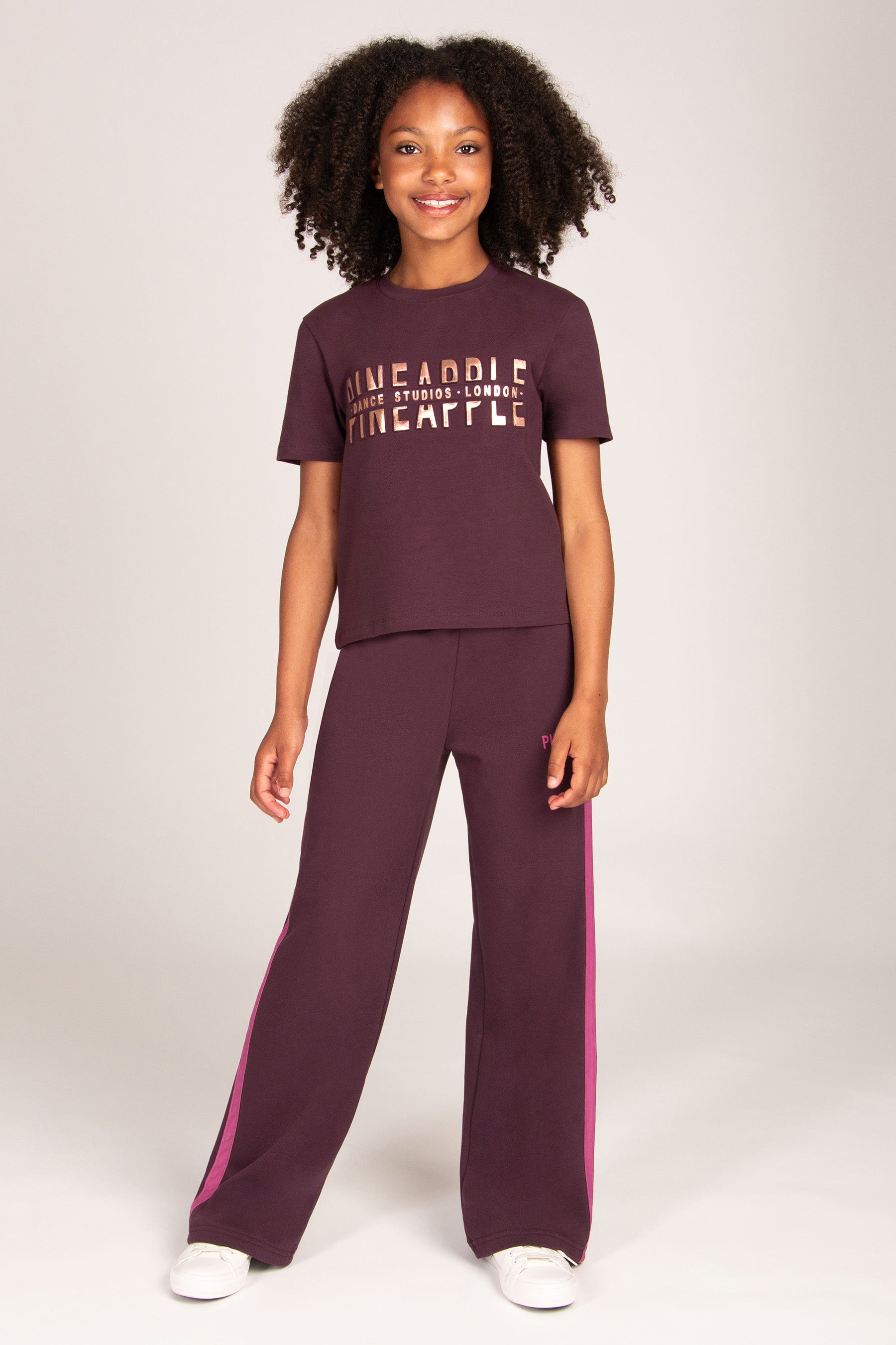 Girl wearing maroon brown trousers with pink side panel and matching t-shirt on a plain background