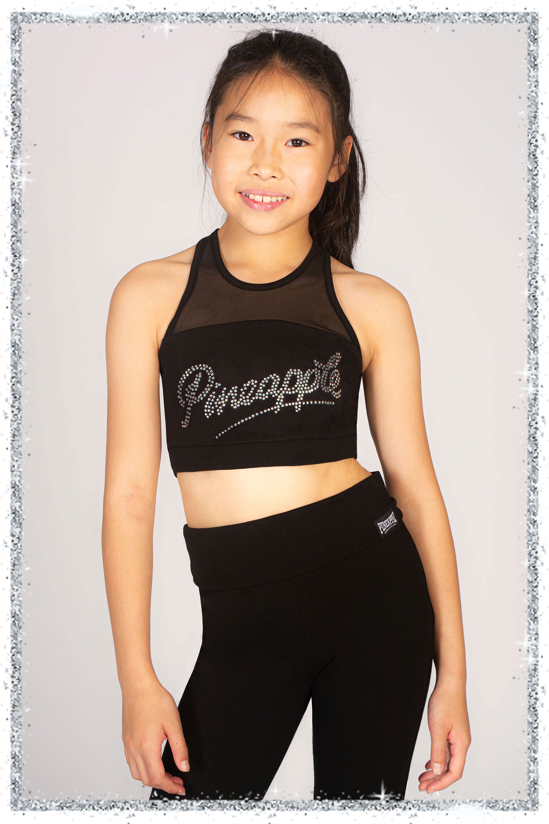Young girl wearing a black 'Pineapple' sports bra and leggings on a light gray background