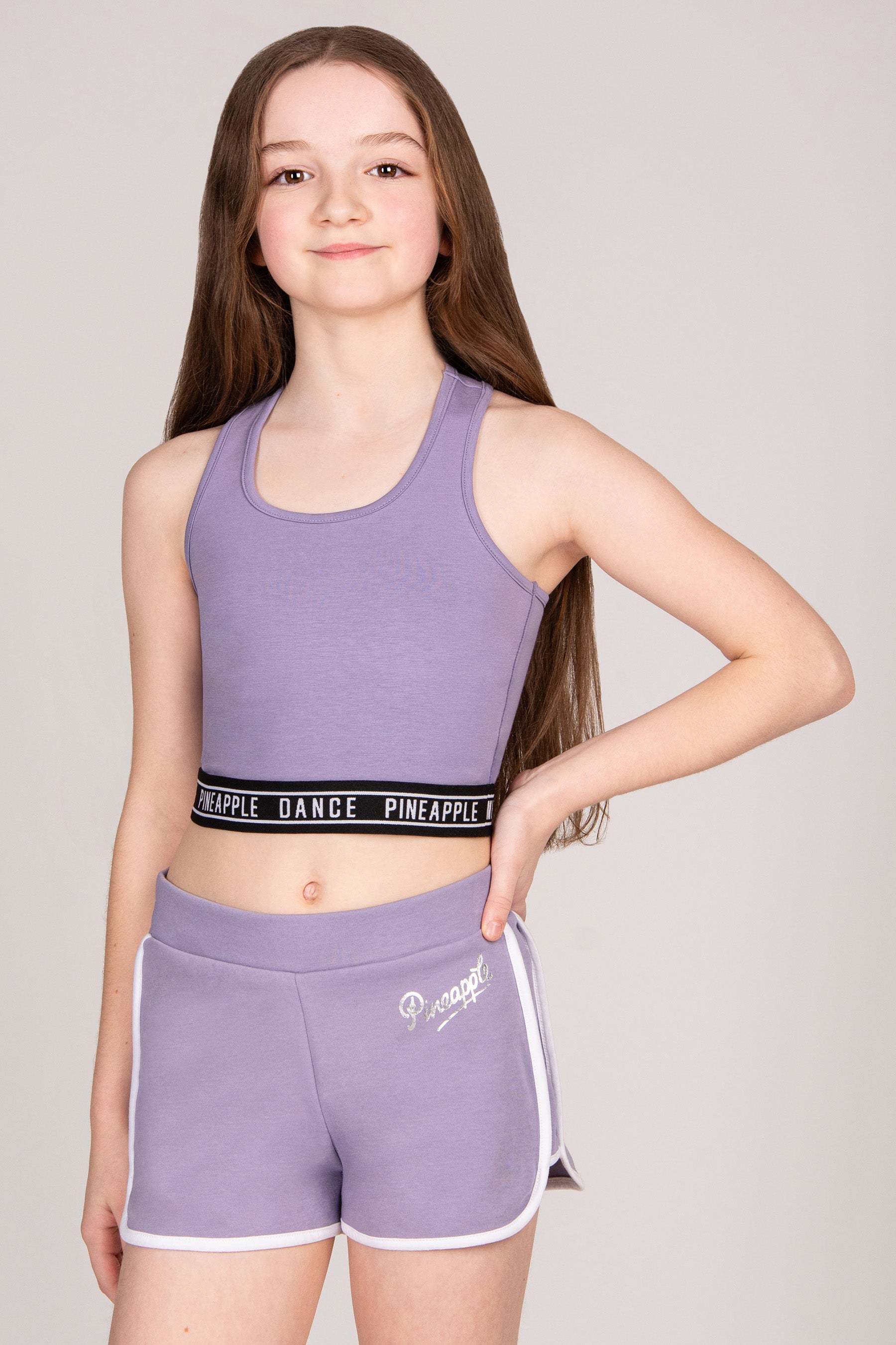 Young girl wearing a purple crop top and shorts set with 'Pineapple Dance' branding on a plain background.