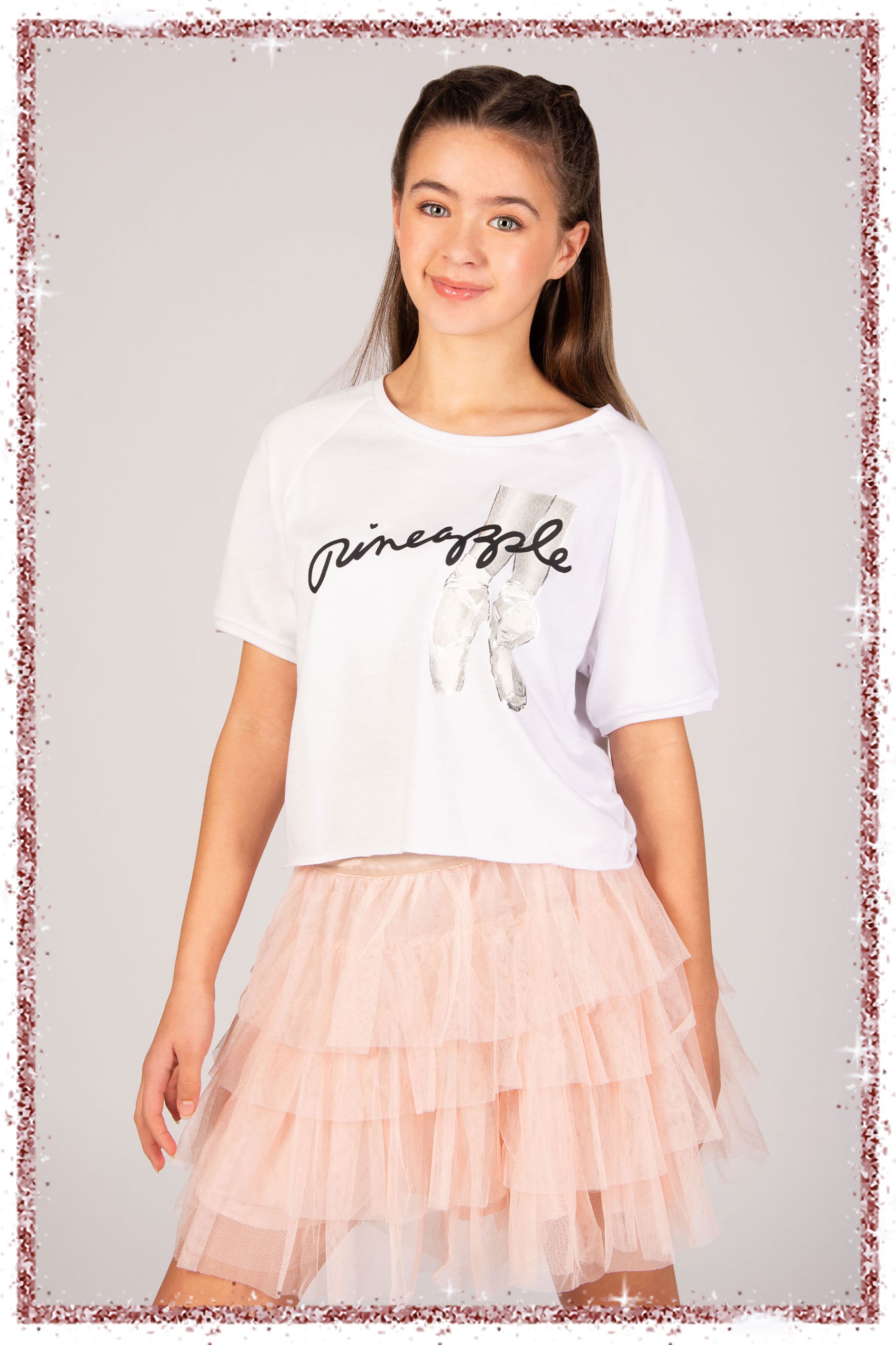 Girl wearing a white t-shirt with ballet pointe shoe graphics and a pink tutu skirt