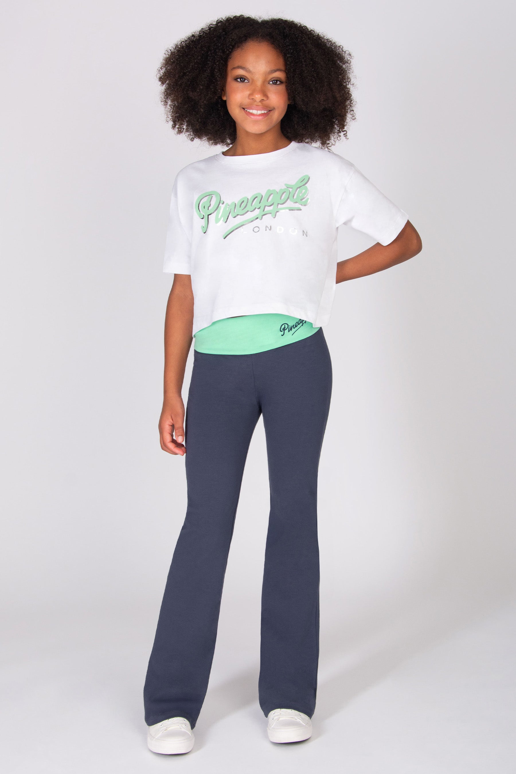 Teen wearing a white t-shirt and dark grey flared trousers on a white background