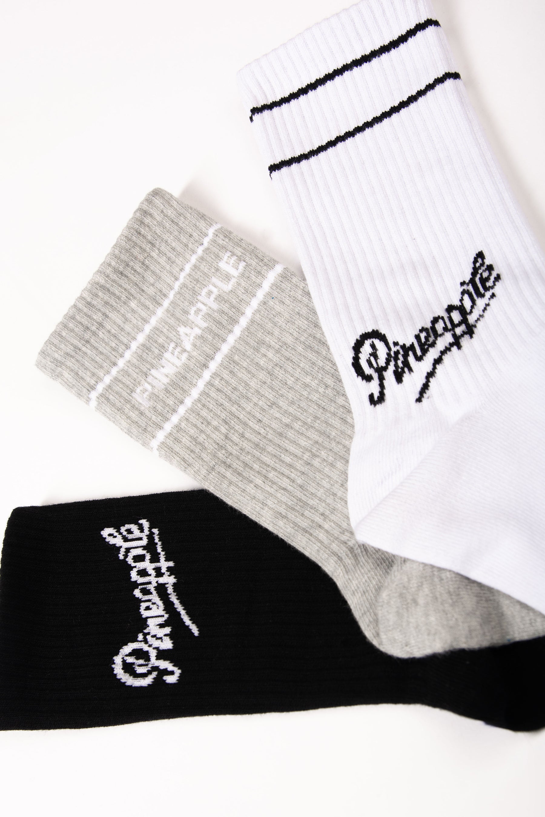 Three socks in white, gray, and black with 'Pineapple' branding on a light background.