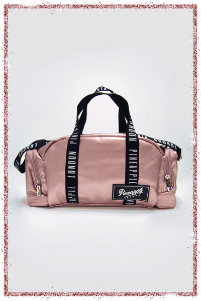 Pink duffel bag with black straps and a brand label on a white background