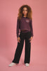 Girl wearing a maroon brown hoodie with matching black wide leg trousers against a pink background