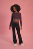 Girl wearing a maroon brown long-sleeve crop top and matching black flared trousers on a pink background