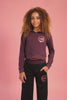 Girl wearing a maroon brown hoodie with matching black wide leg trousers against a pink background