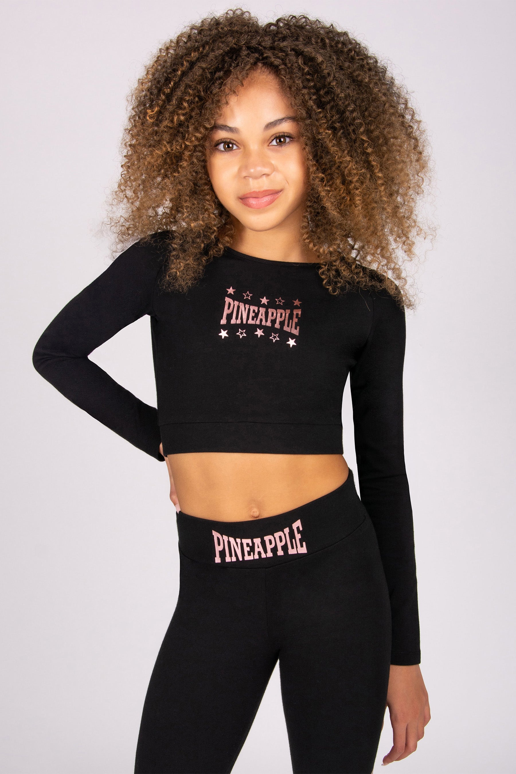 Girl wearing a black long-sleeve crop top and leggings with 'Pineapple' branding on a plain background