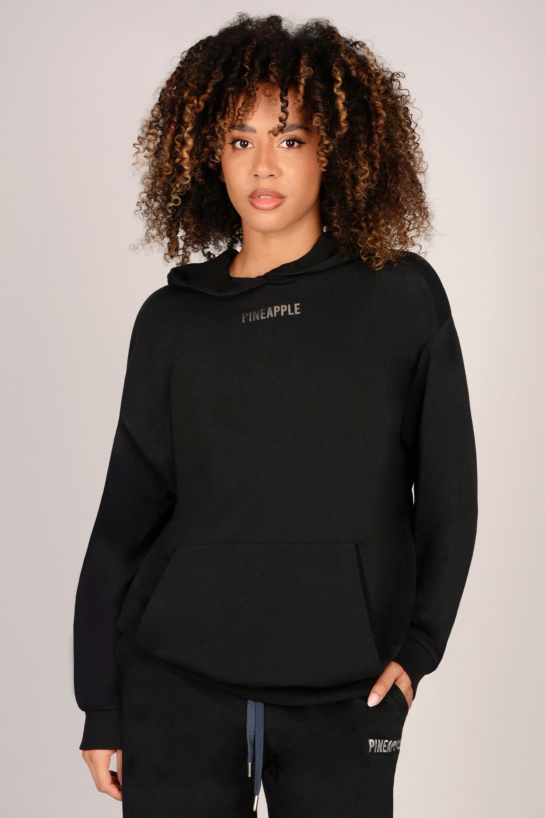Woman wearing a black hoodie with 'Pineapple' branding on a plain background