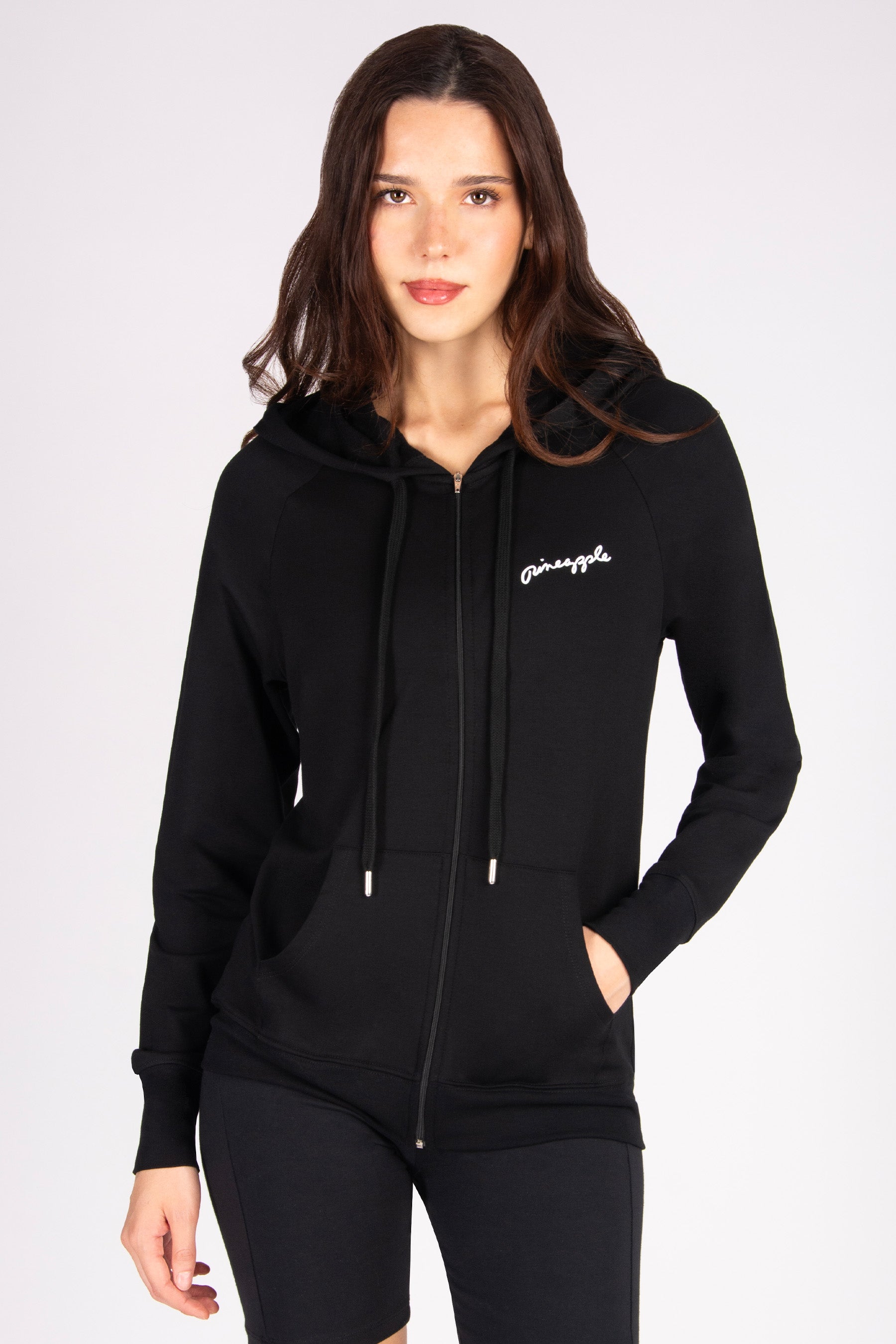 Woman wearing a black hoodie with a front pockets and zip on a white background
