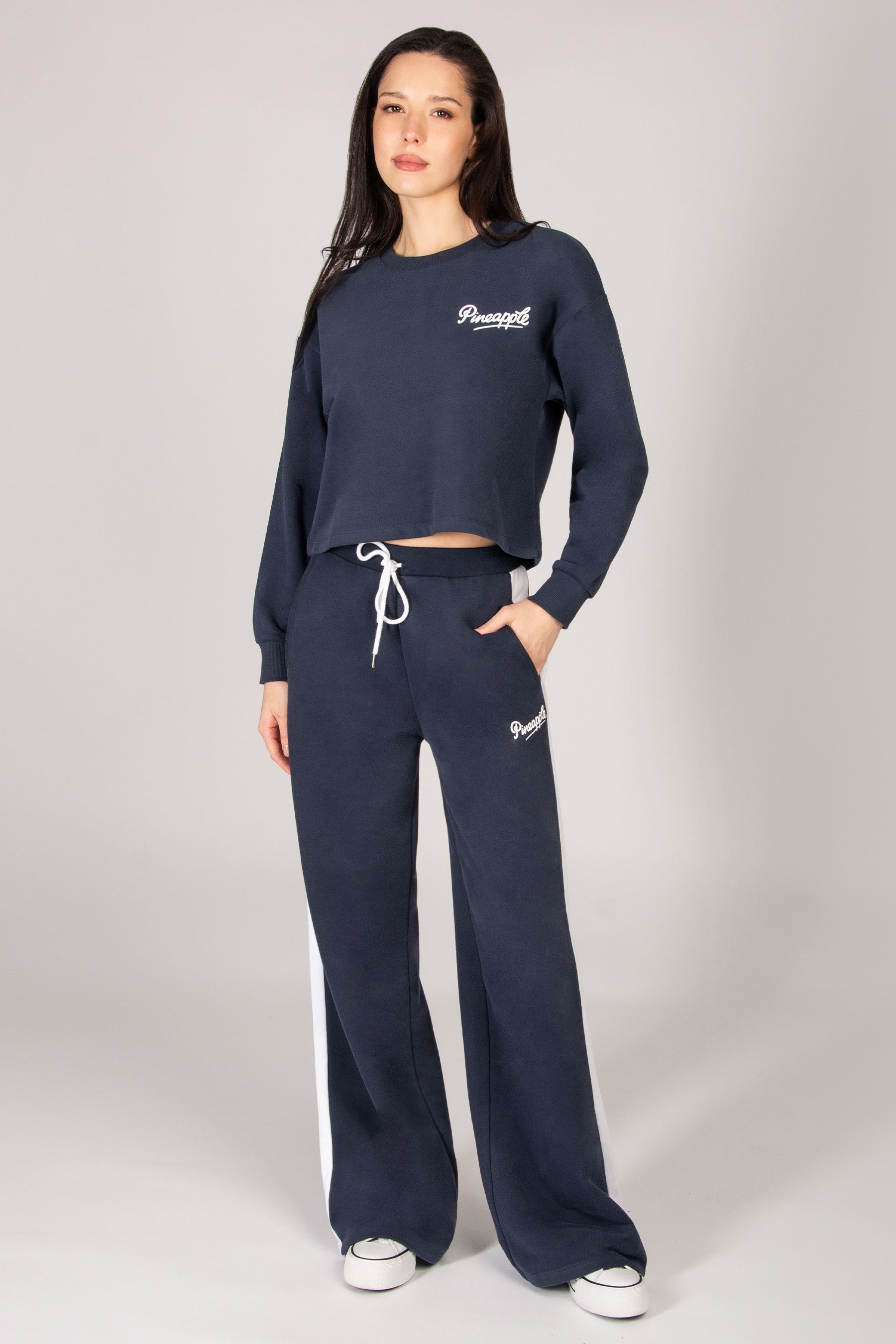 Woman wearing dark blue midi sweatshirt and matching wide leg trousers on a light grey background