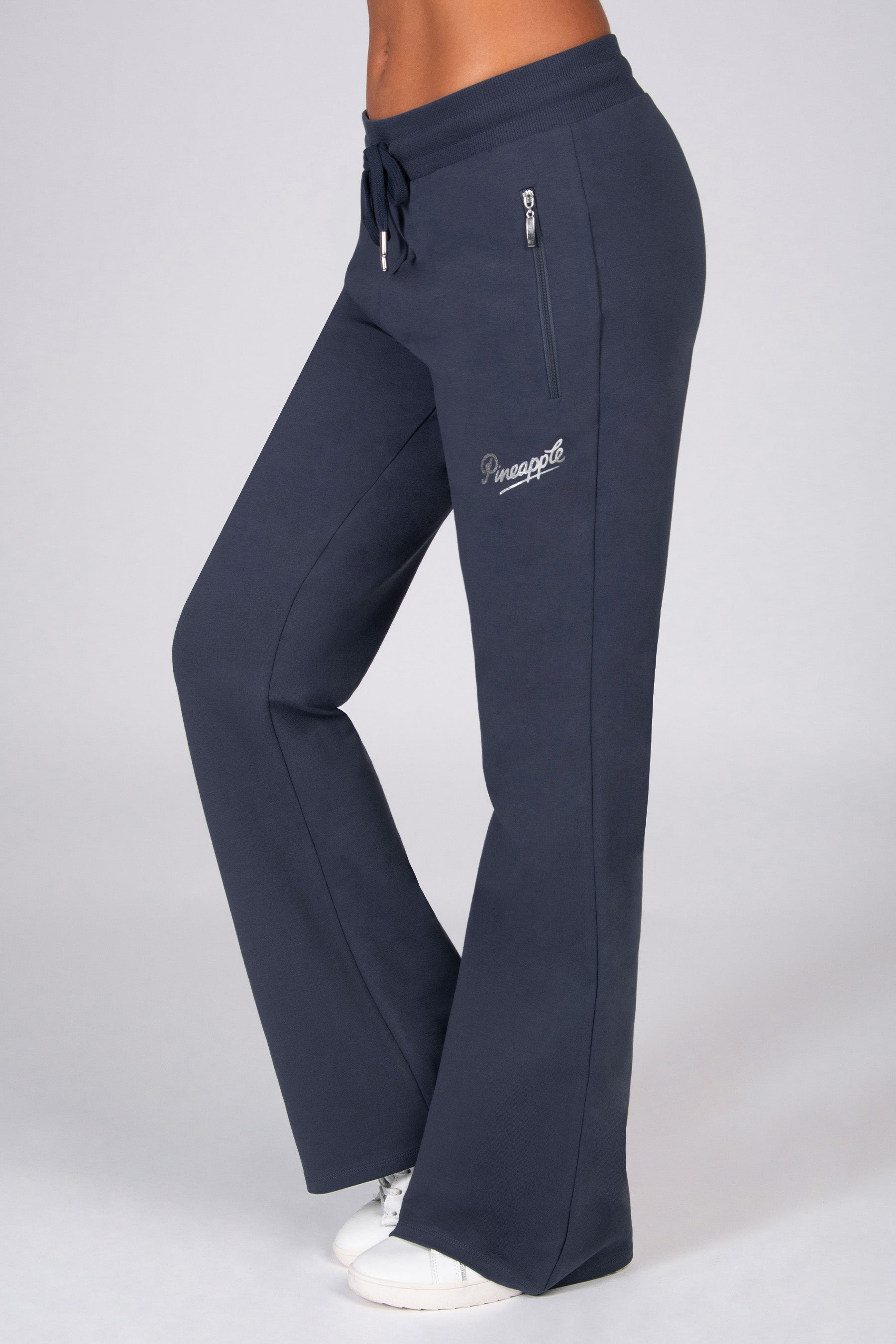 Dark grey flared trousers with zip pockets worn by a person on a light grey background. 