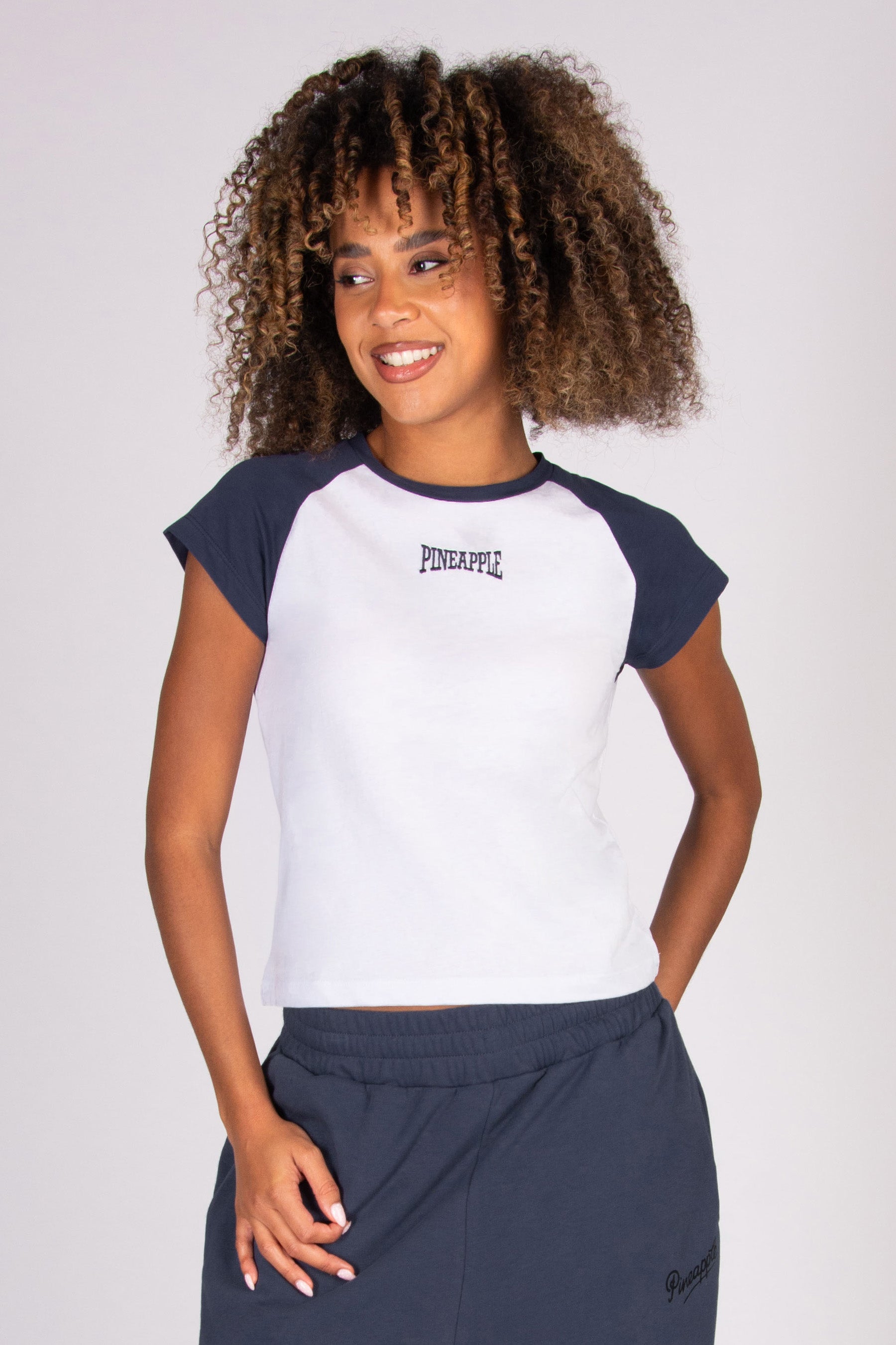 Woman wearing a white t-shirt with dark grey raglan sleeves on a plain background