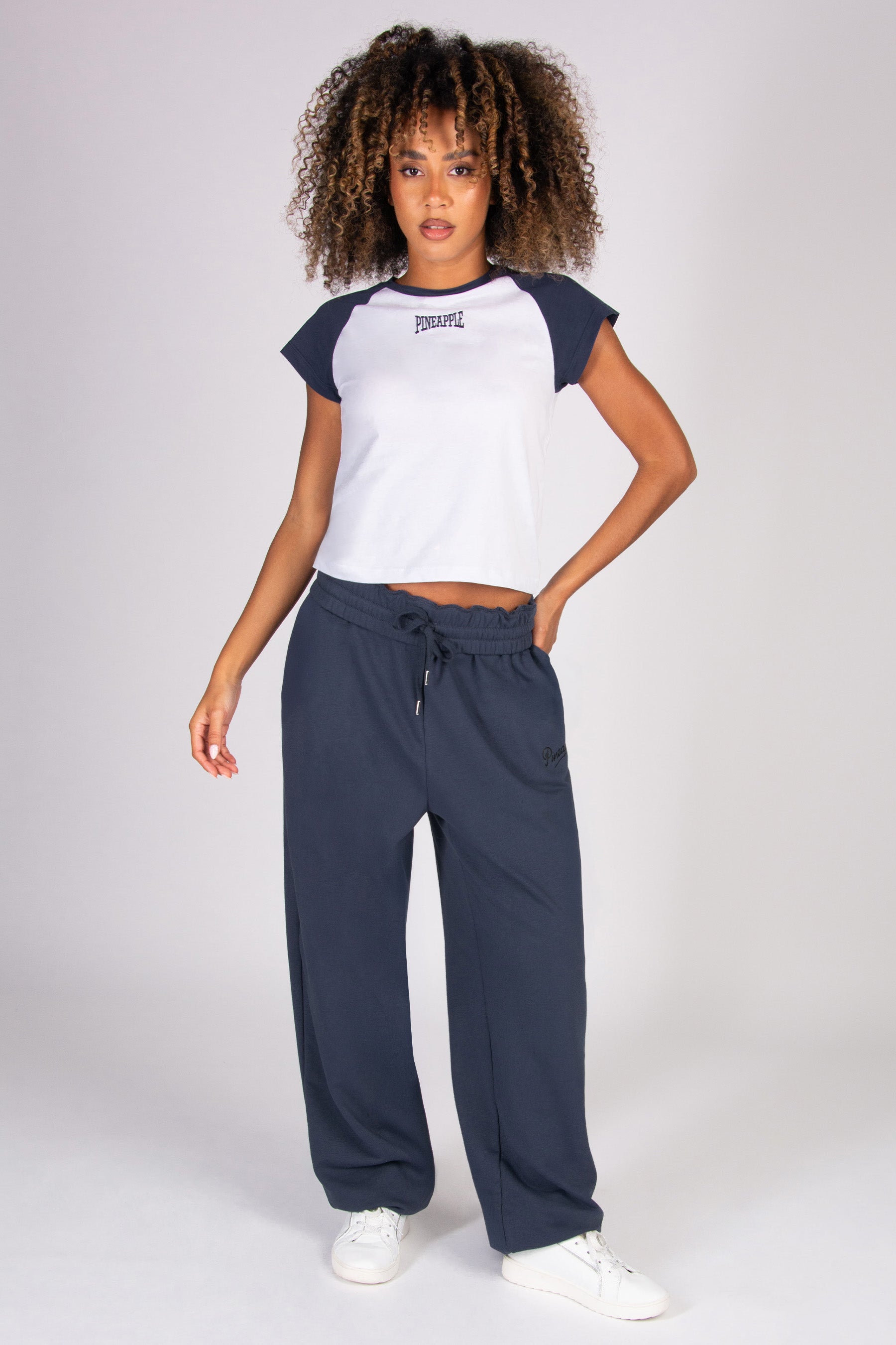 Woman wearing a white t-shirt with dark grey raglan sleeves and oversized dark grey joggers on a plain background