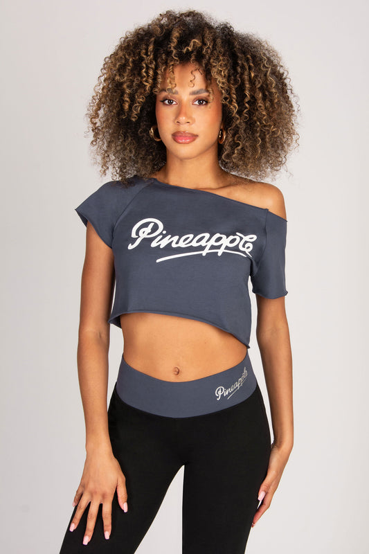 Woman wearing a dark grey off-shoulder top and black leggings with 'Pineapple' branding on a light grey background