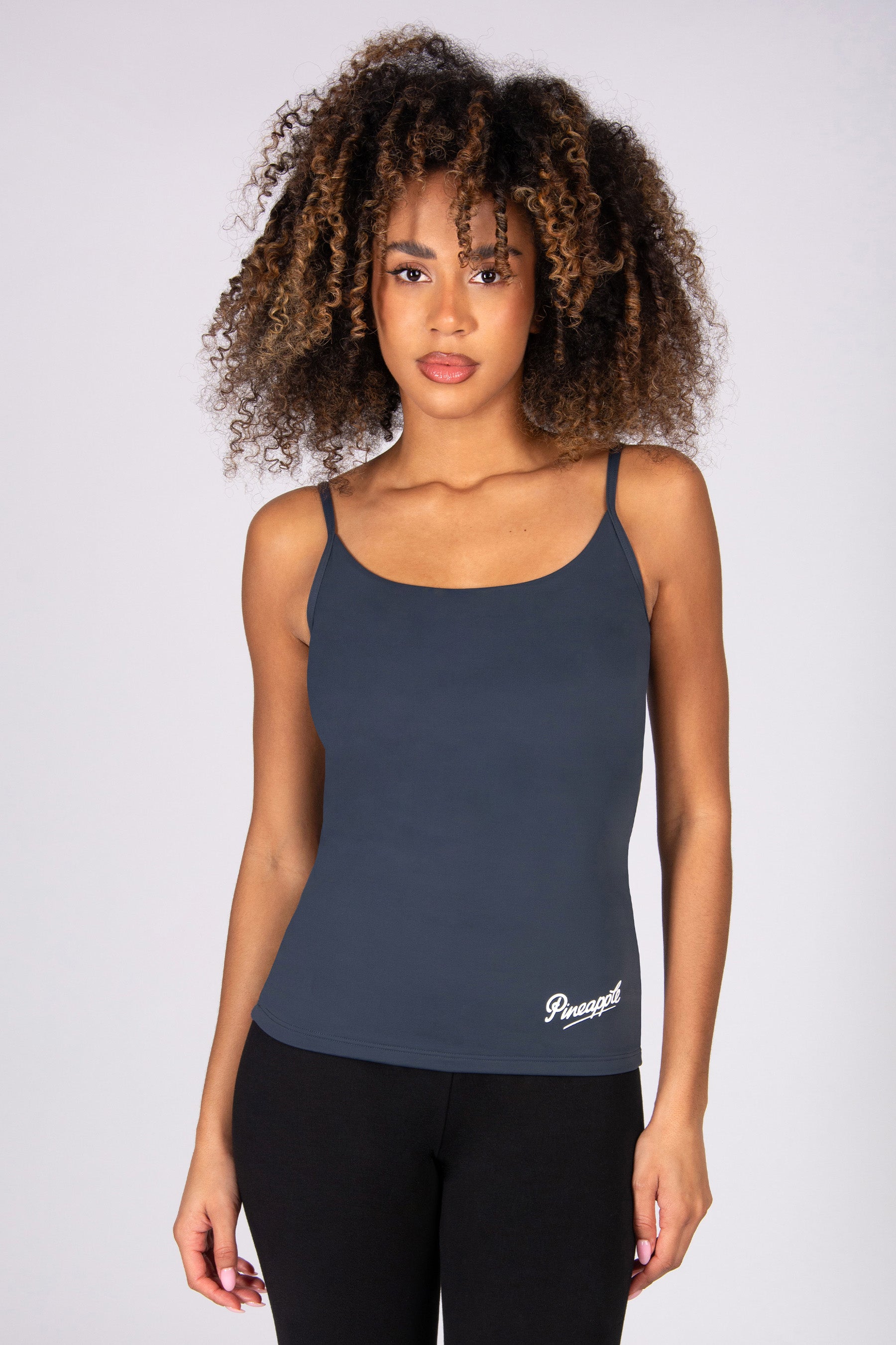 Woman wearing a dark grey tank top with adjustable straps on a plain background