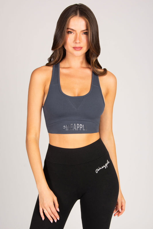 Woman wearing a grey sports bra and black leggings with minimal branding on a plain background