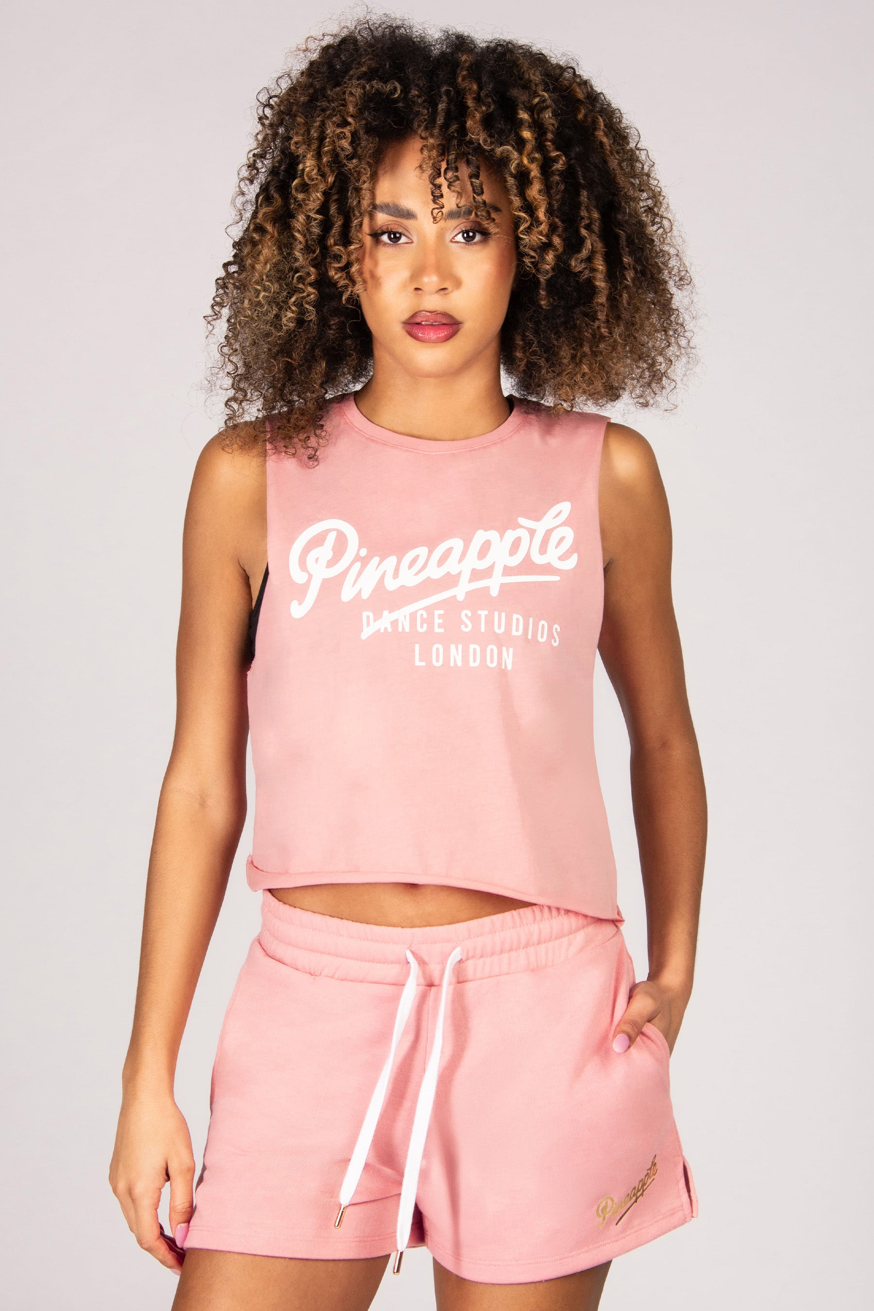 Woman wearing a light pink sleeveless top and shorts with 'Pineapple Dance Studios London' branding.
