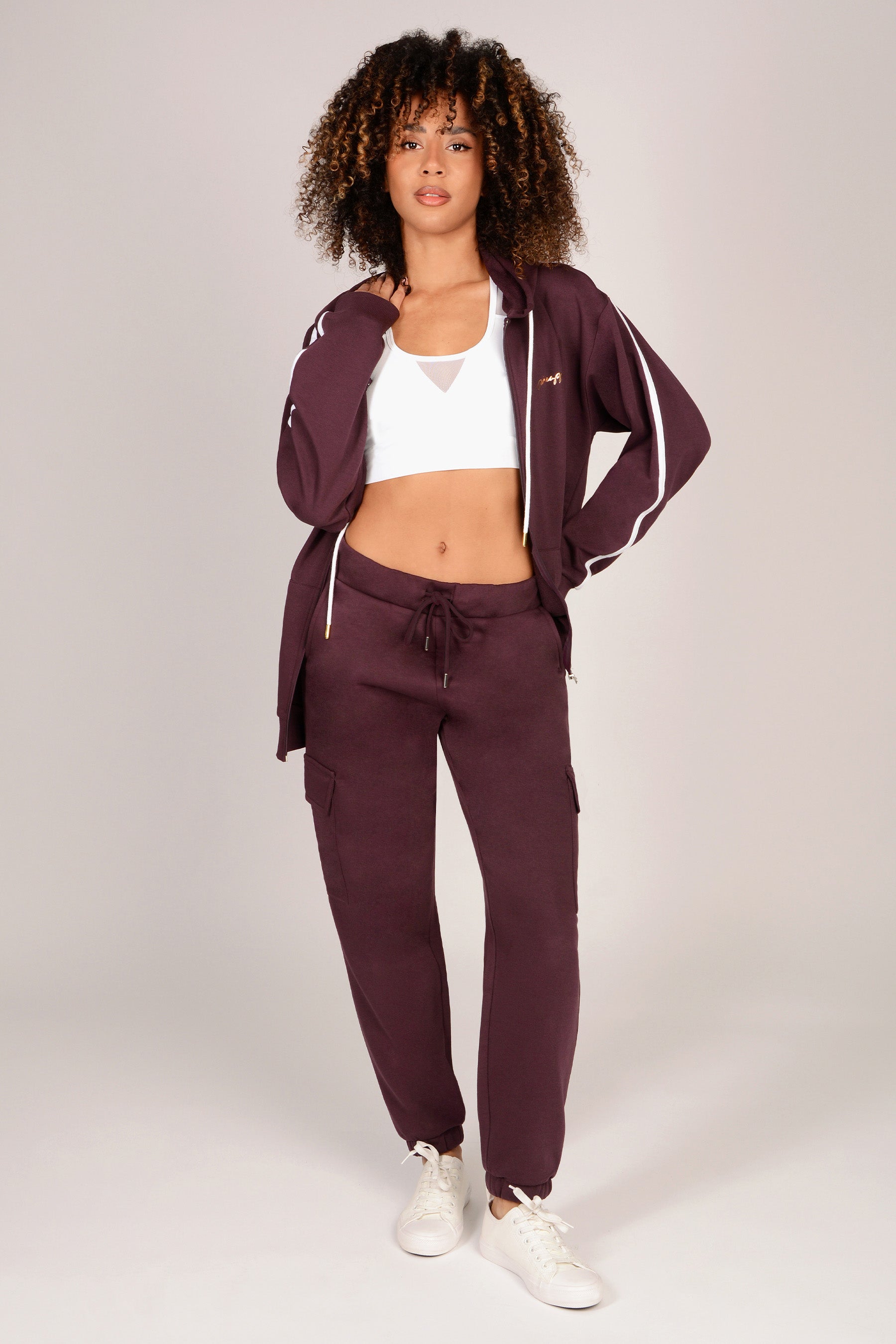 Woman wearing a maroon brown cargo joggers with white accents on a plain background