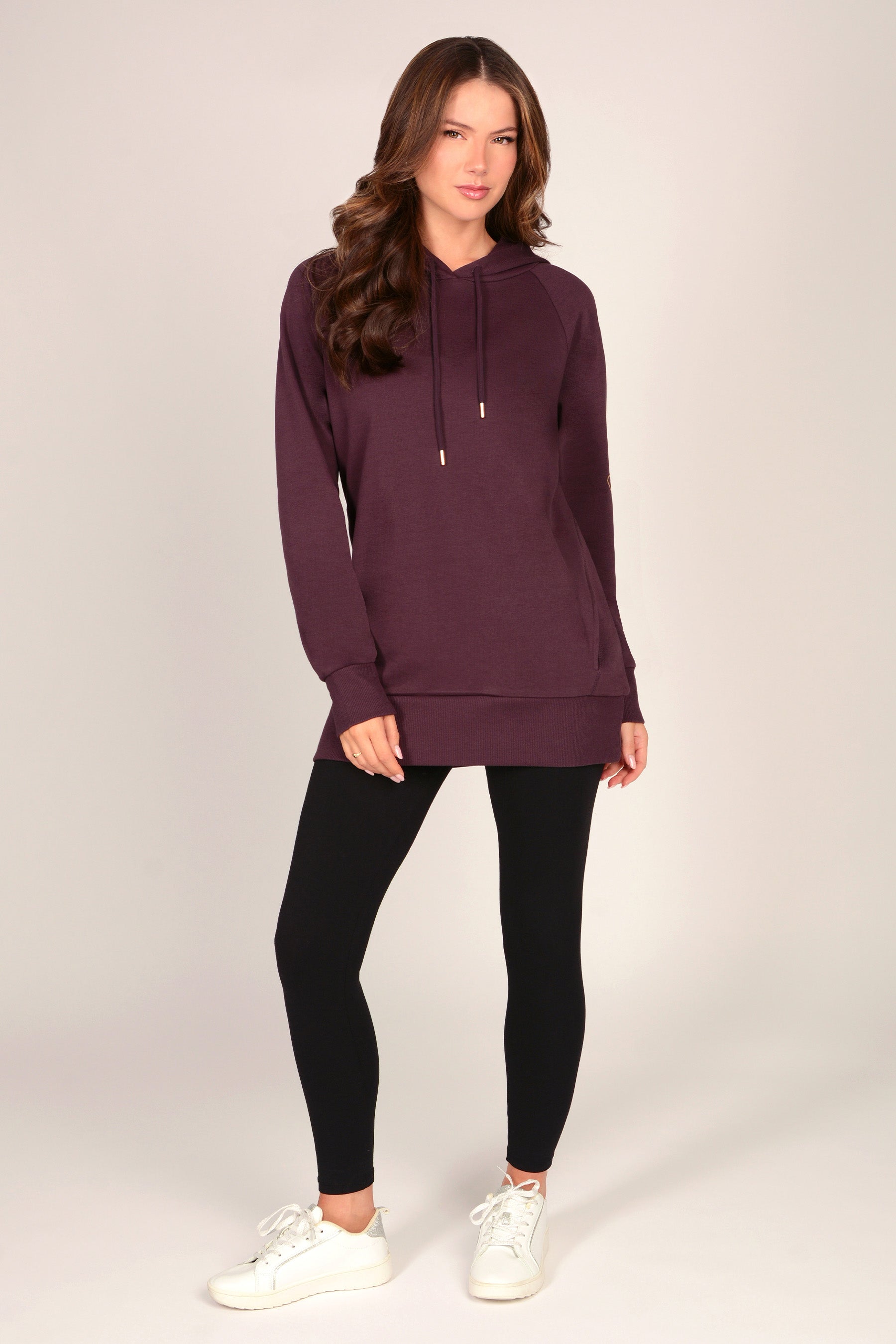 Woman wearing a maroon brown hoodie with black leggings against a grey background