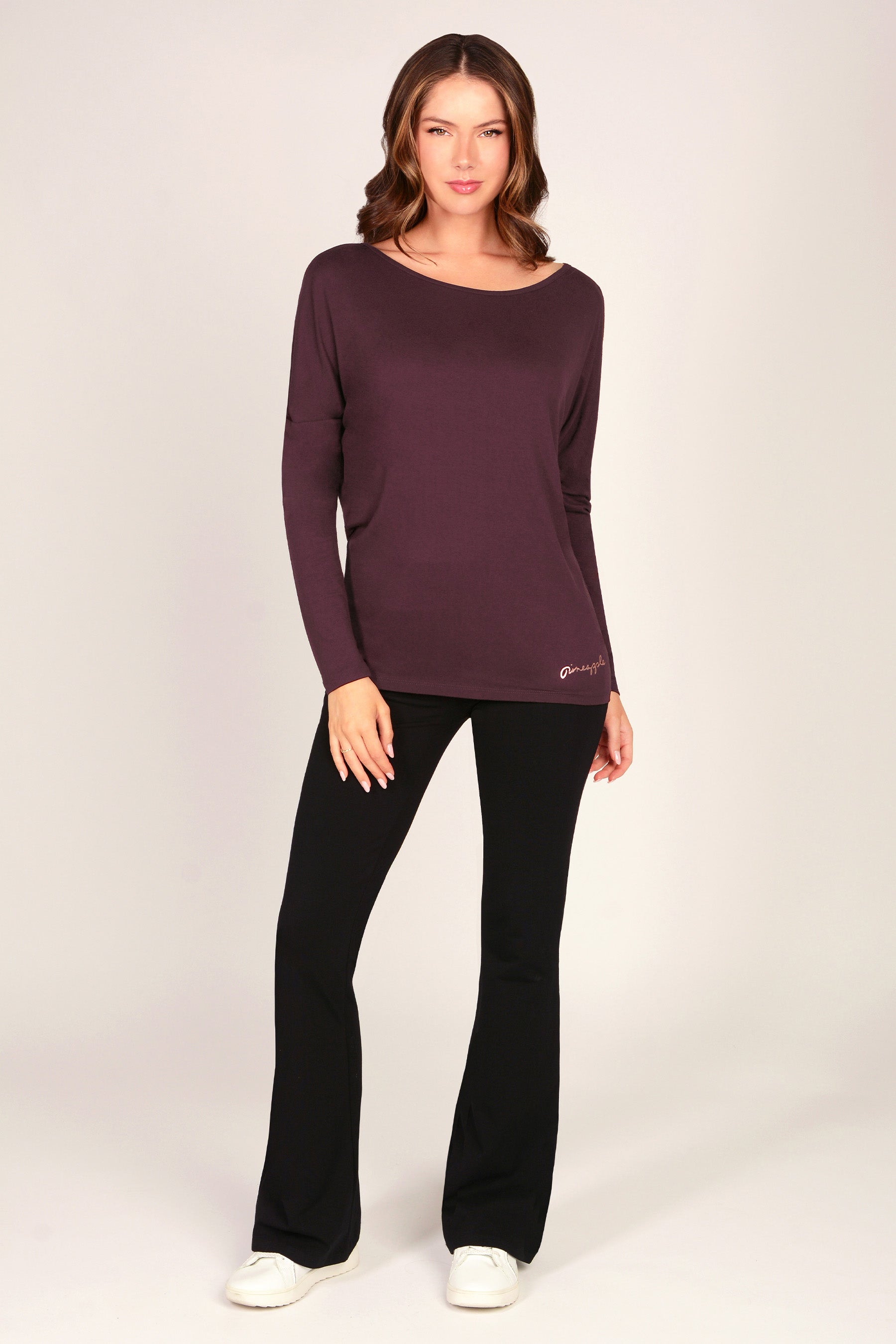 Woman wearing a maroon brown long sleeve tunic top with black flared trousers on a grey background.