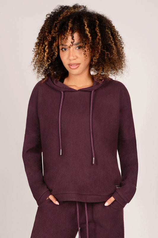 Woman wearing a maroon hoodie and matching trousers on a plain background