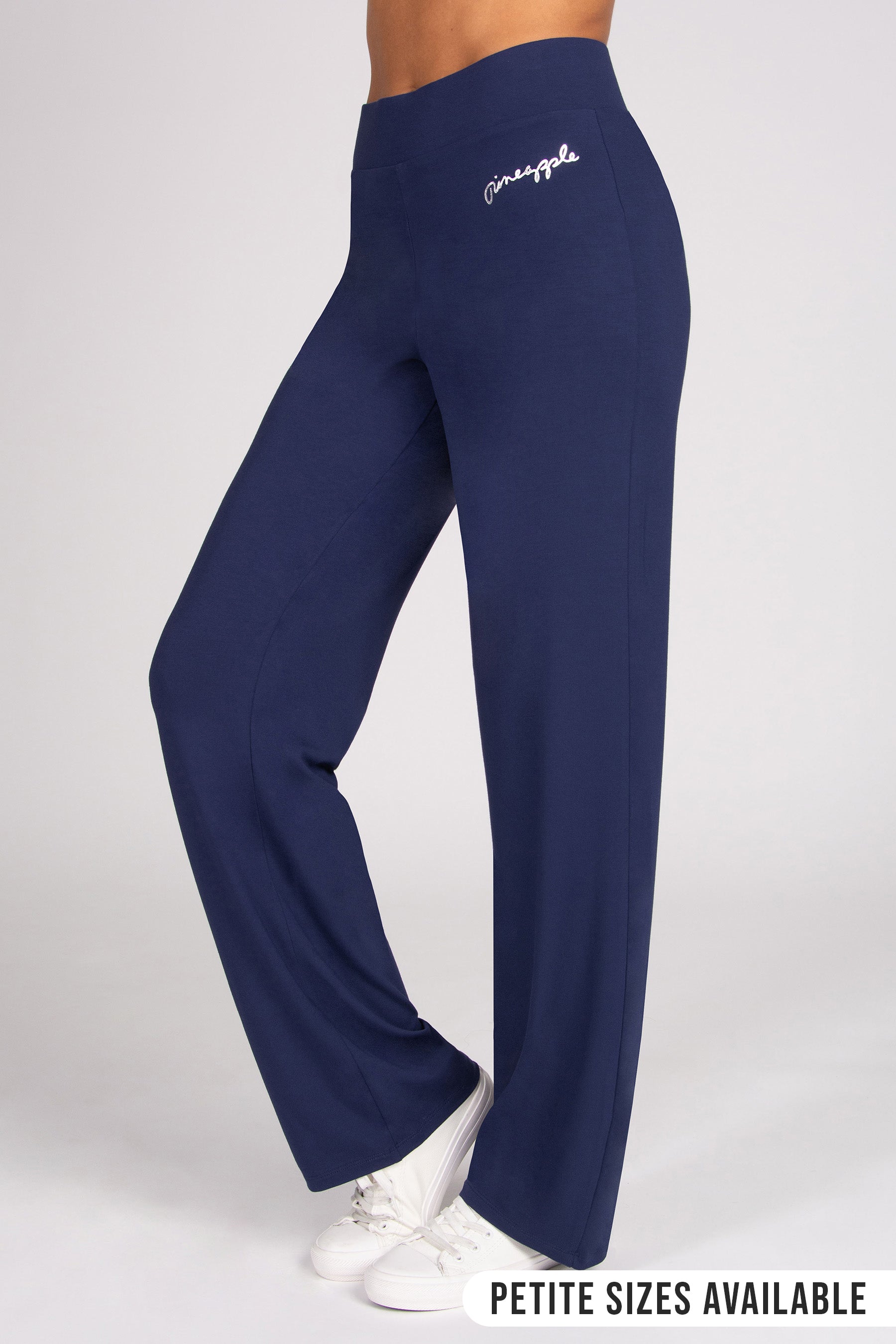 A person wearing navy blue wide-leg pants with white trainers, shown from the waist down against a light grey studio background.
