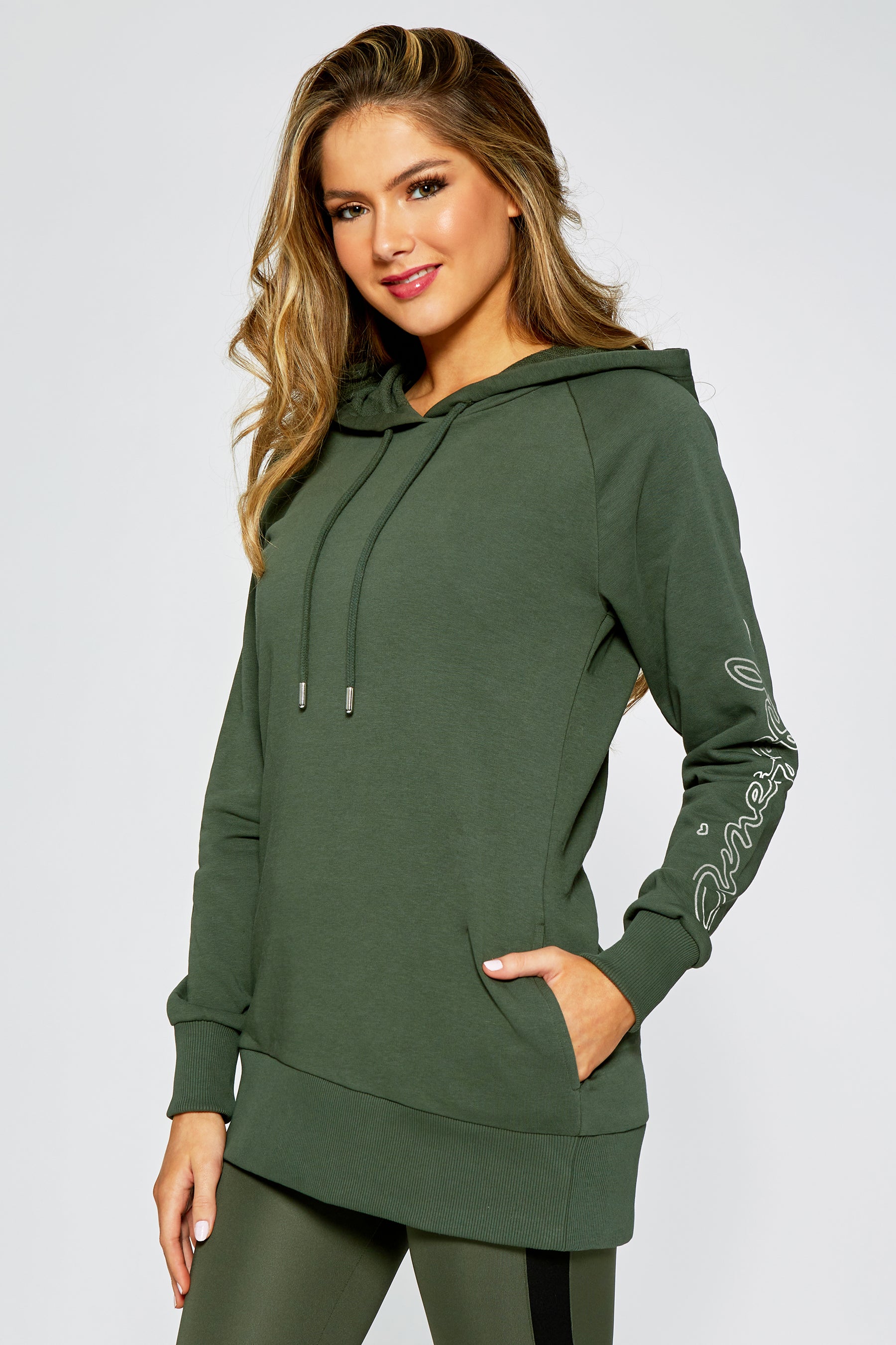 Woman wearing a khaki pocket hoodie against a light gray background