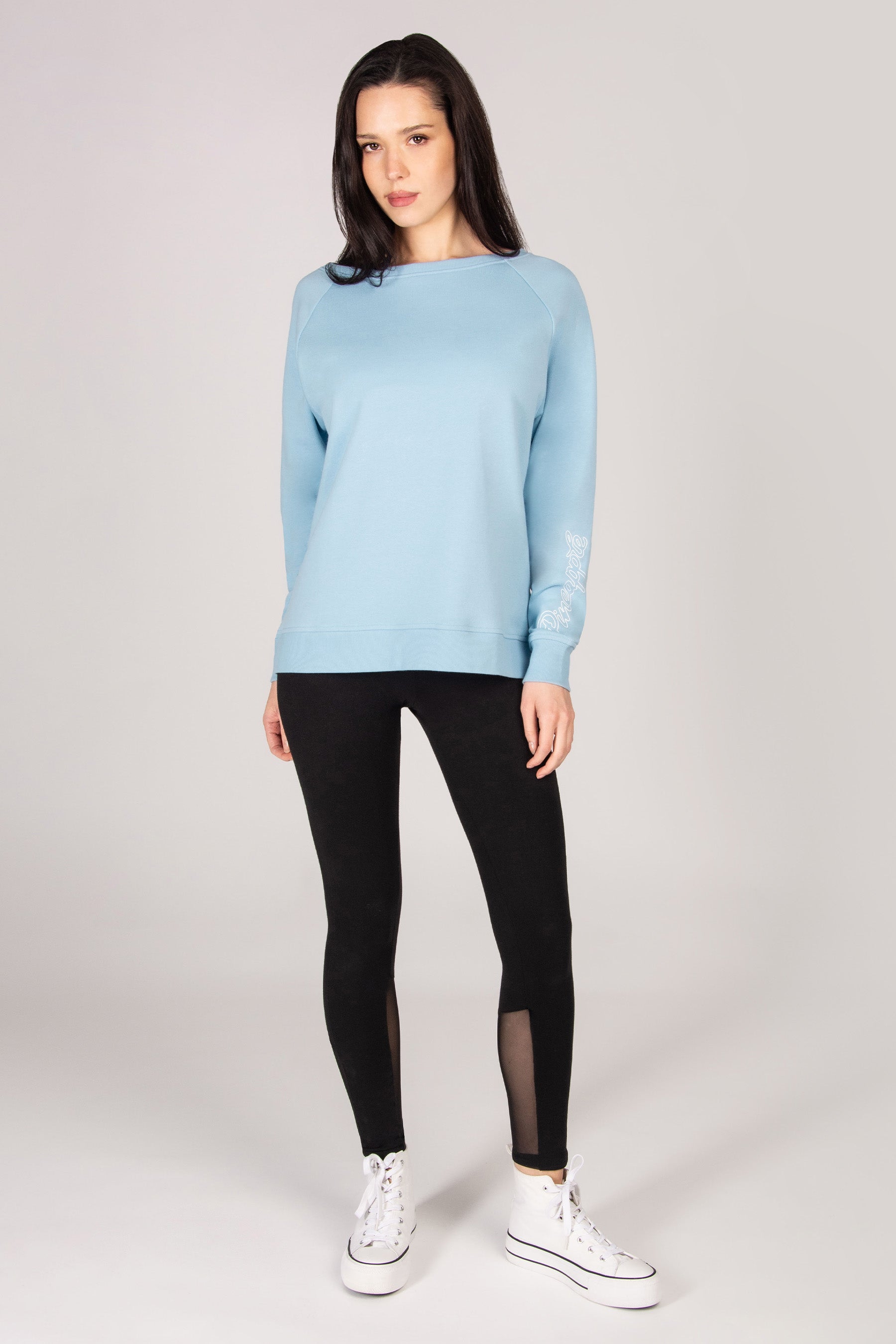 Woman wearing a light blue sweatshirt and black leggings on a white background