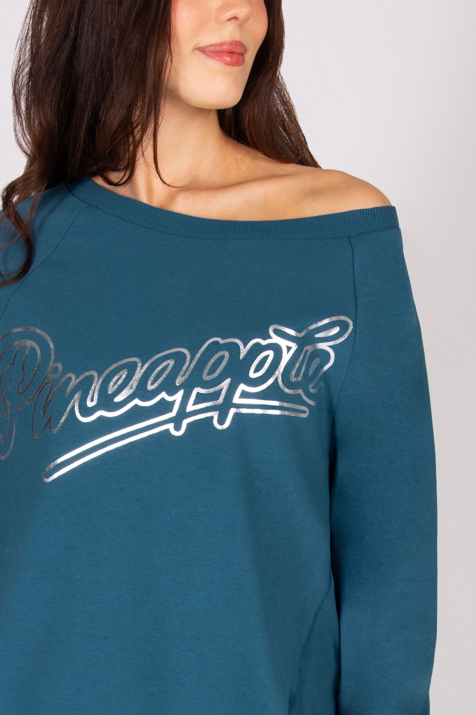 Detail of the 'Pineapple" logo print on a teal sweat top. 