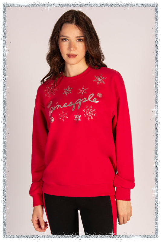 Woman wearing a red sweatshirt with snowflake designs and the word 'Pineapple' on a plain background