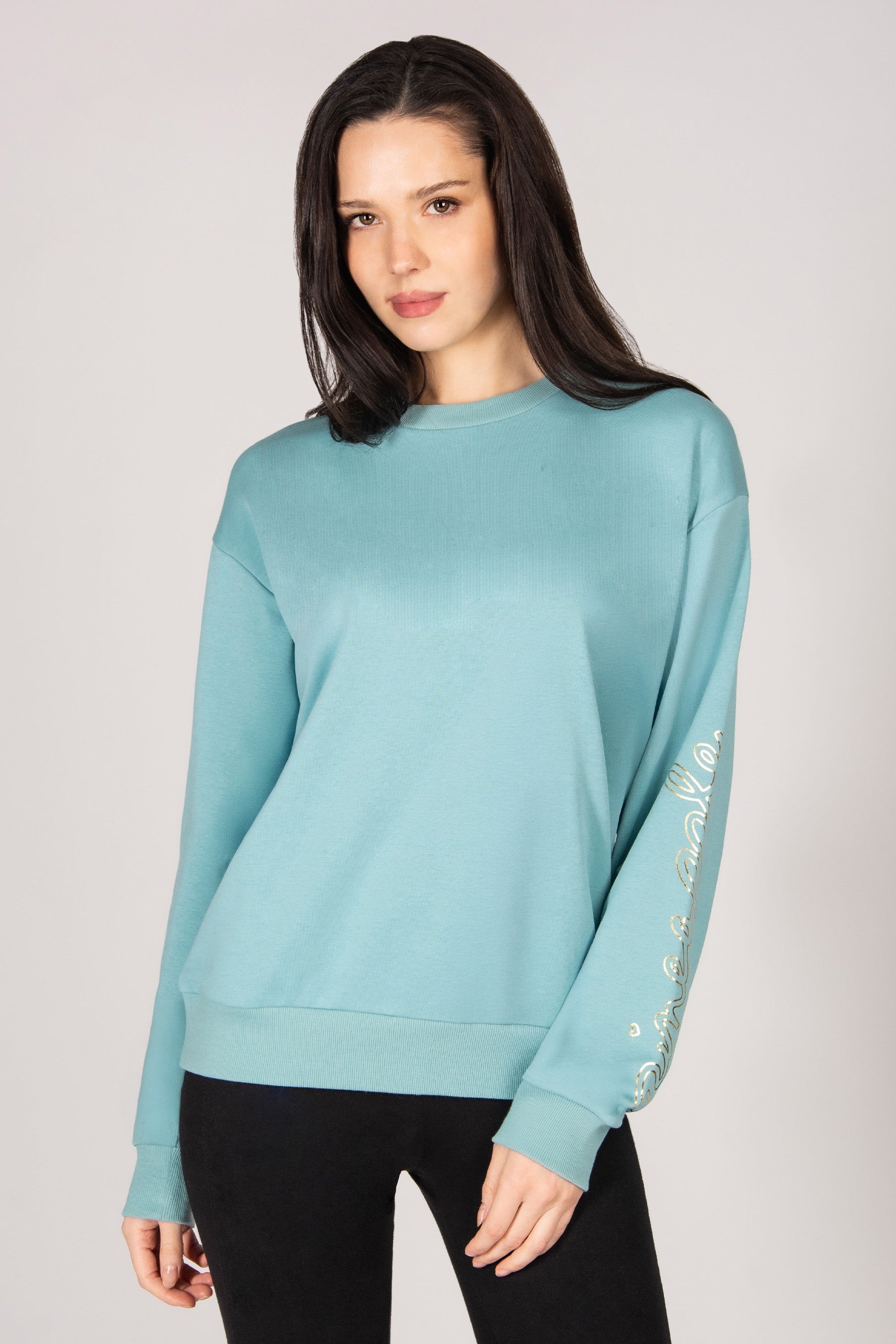 Woman wearing a light blue sweater with decorative sleeves on a plain background