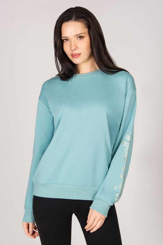 Woman wearing a light blue sweater with decorative sleeves on a plain background