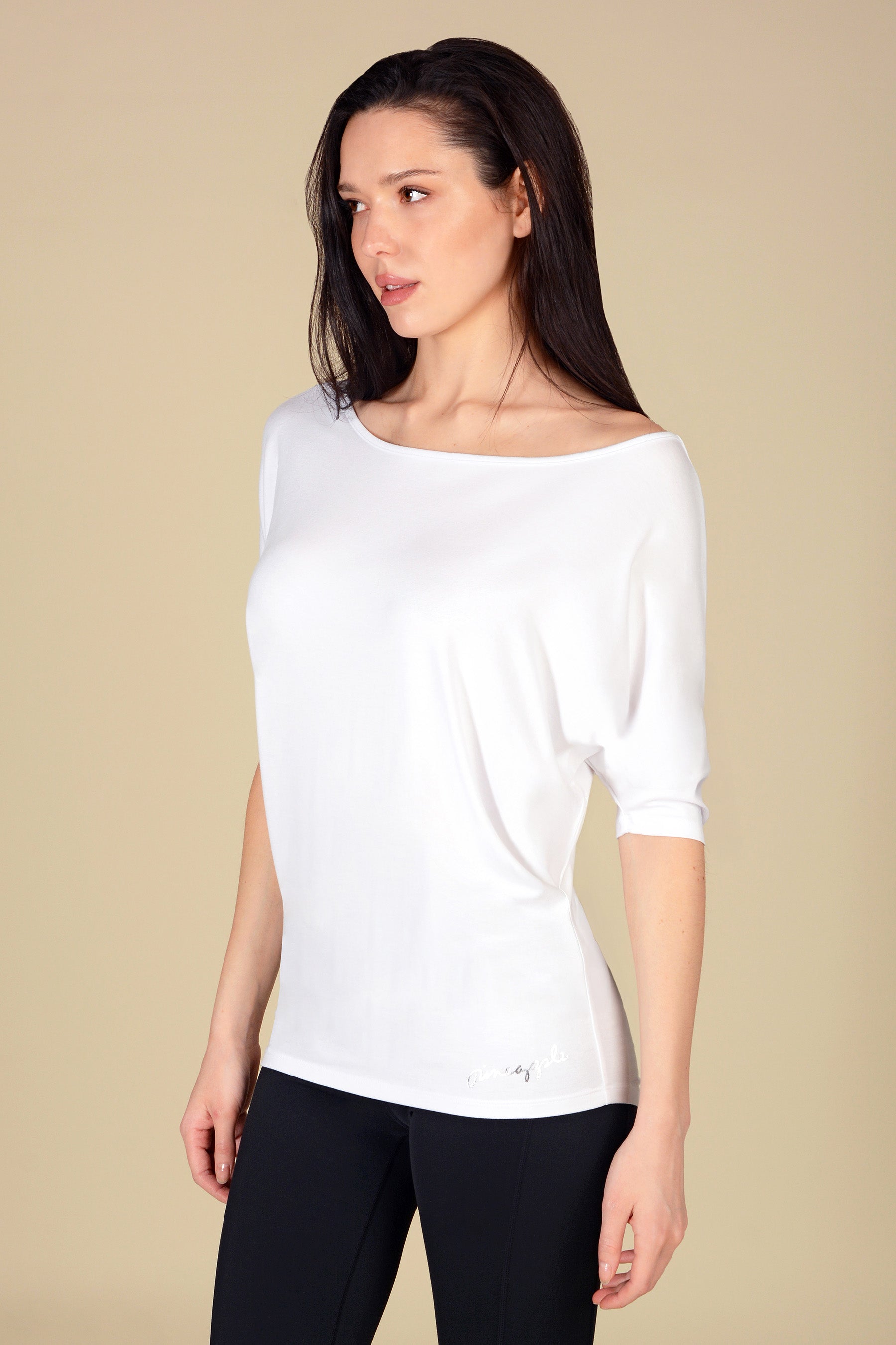 Woman wearing a white top and black leggings against a beige background